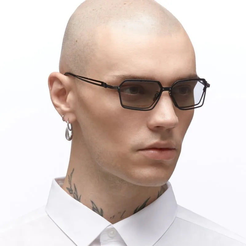 Man with a shaved head wearing black sunglasses and a white shirt on a white background