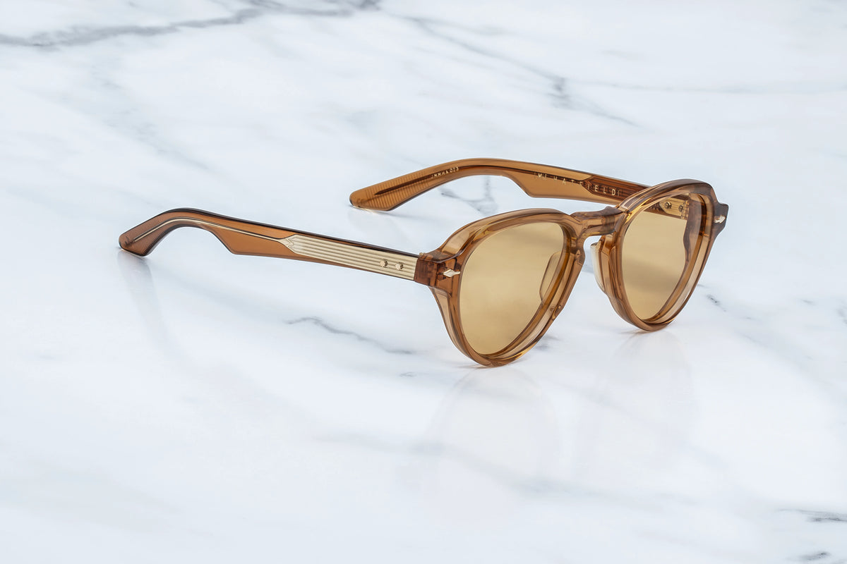 Translucent amber-colored Jacques Marie Mage Hatfield photochromic sunglasses with gold-toned metal detailing on the temples, resting on a white marble surface.