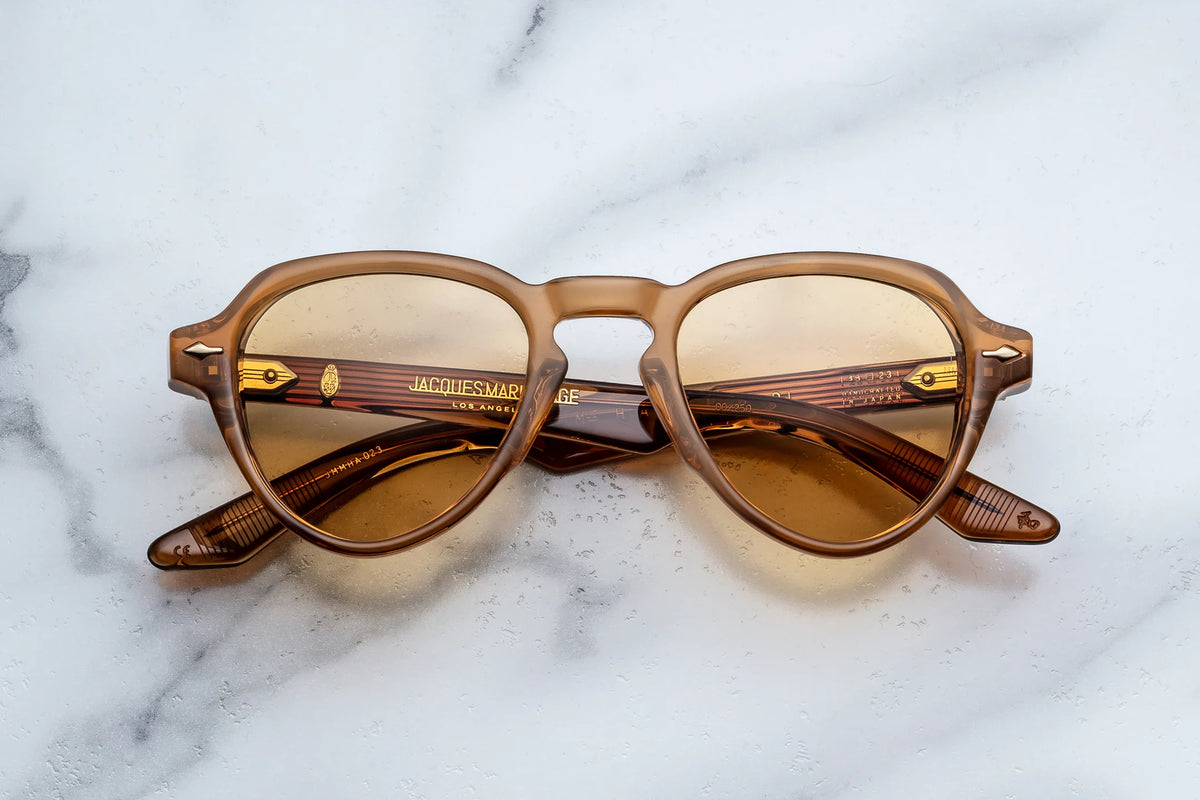 Jacques Marie Mage Hatfield brown-toned, round-frame glasses with light amber photochromic lenses resting on a marble surface, offering versatile UV protection.