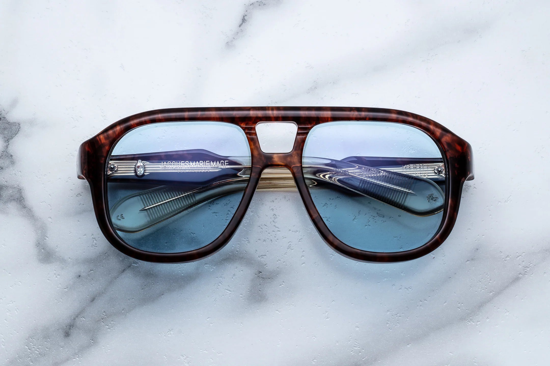 Jacques Marie Mage Sunglasses with reflective lenses on a marble surface