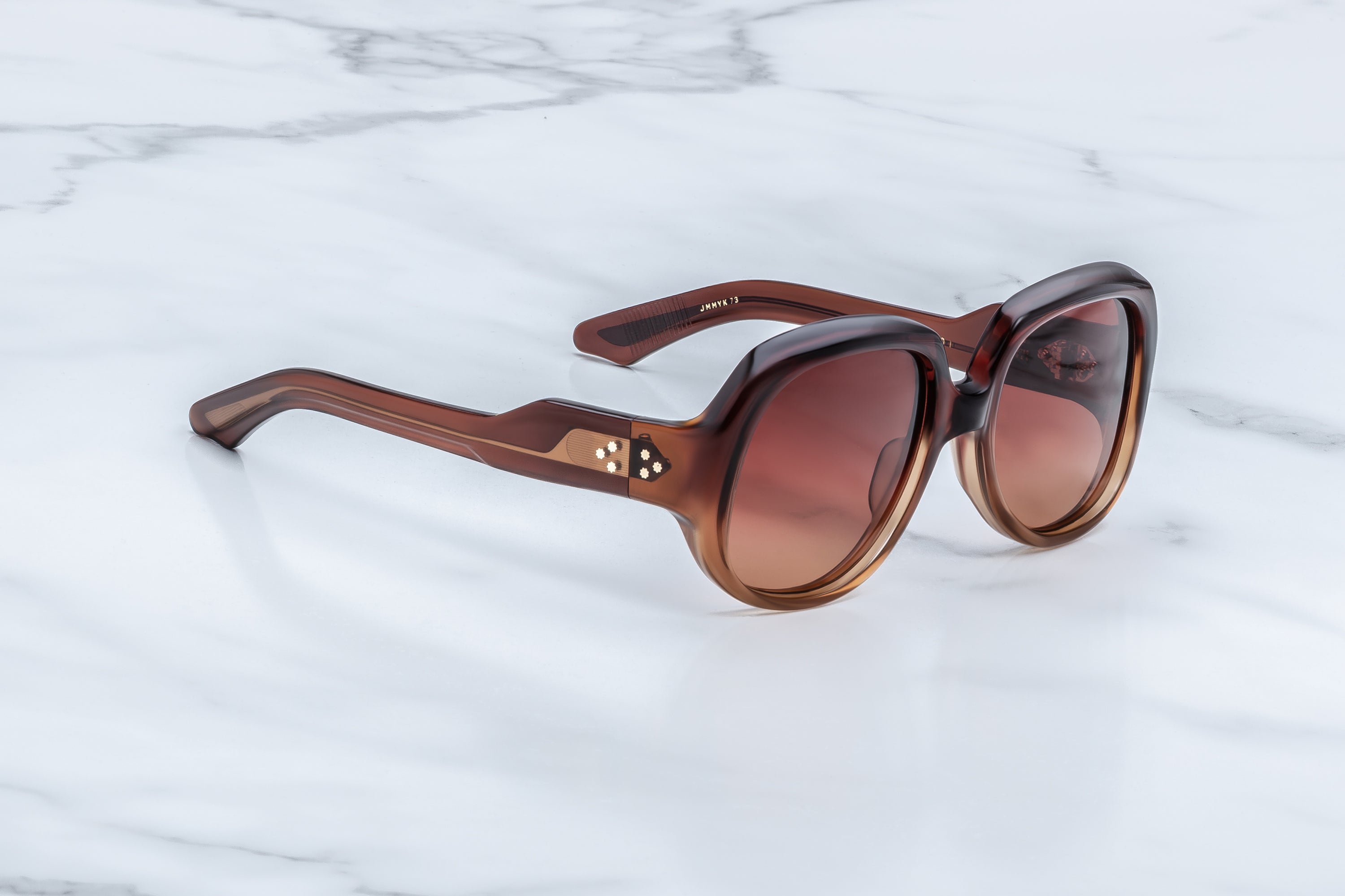 Brown sunglasses with a gold logo on a marble background