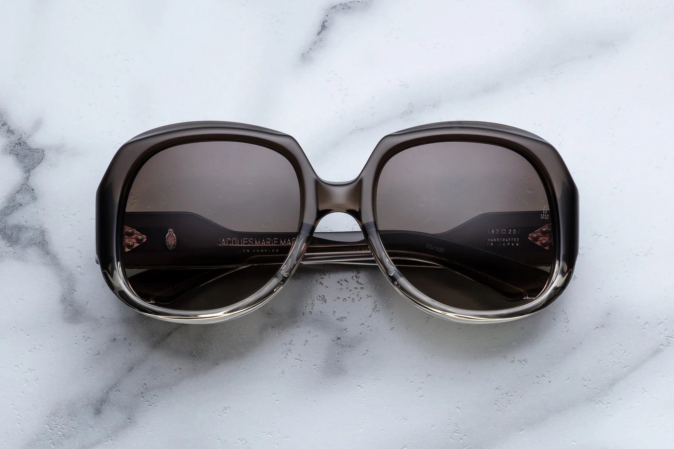 Big Round JMM Sunglasses with dark lenses on a marble surface