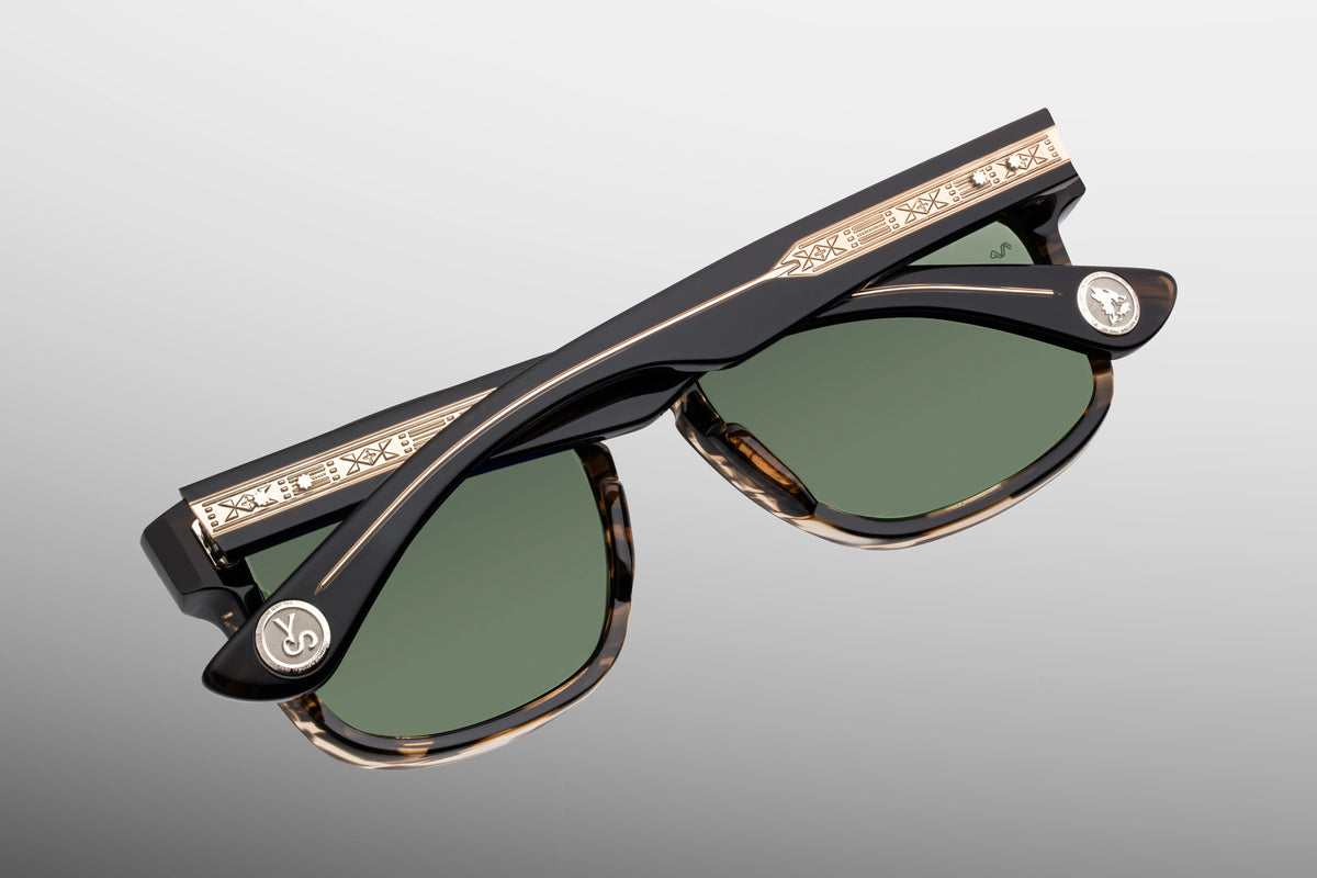 Jacques Marie Mage Yellowstone VII: Junction Butte In Lodgepole handcrafted acetate tortoiseshell sunglasses with green polarized glass lenses, featuring gold-toned temple arms with intricate geometric engravings and circular logos.