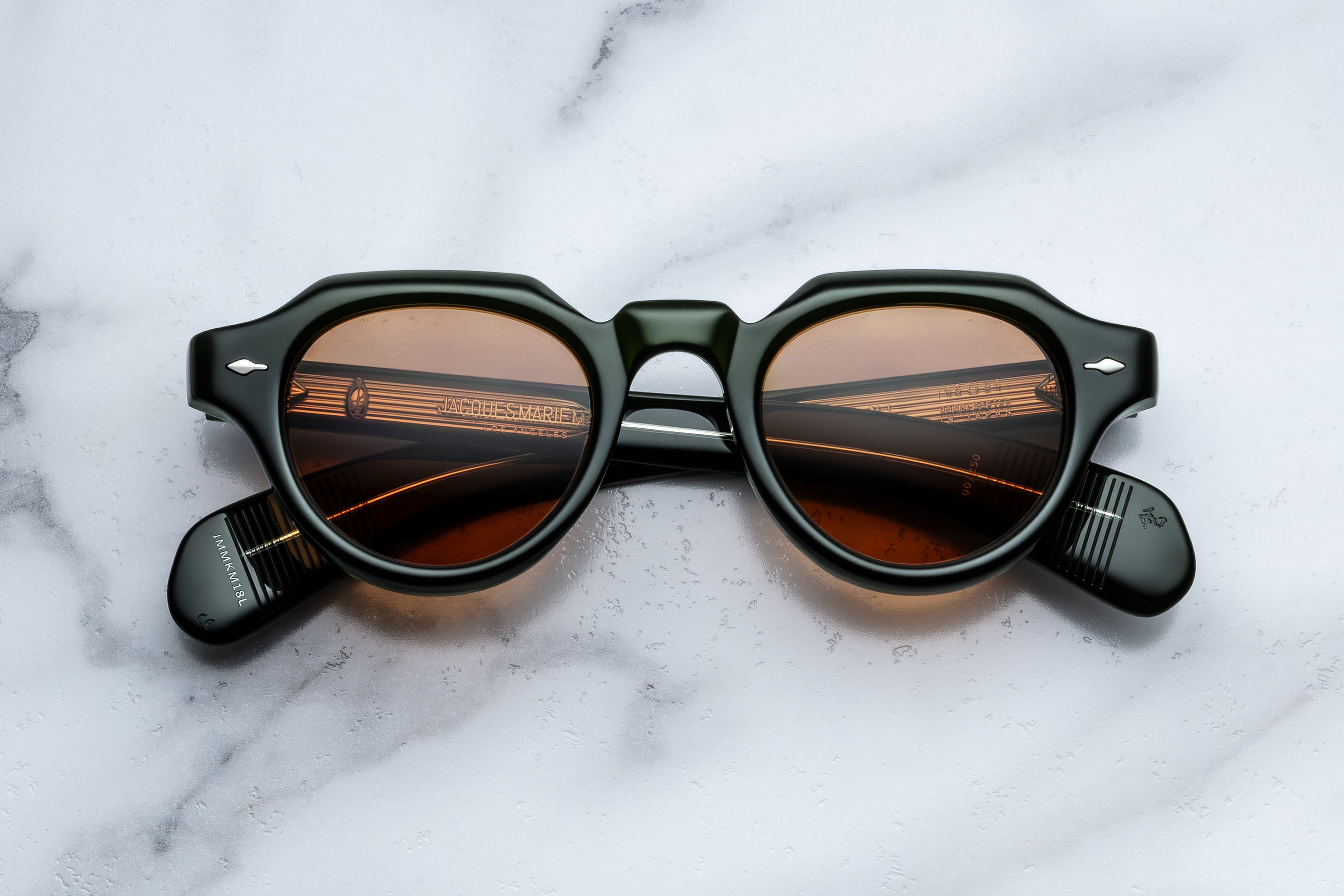 Round sunglasses with thick green frames and amber-tinted lenses, displayed on a white marble surface.