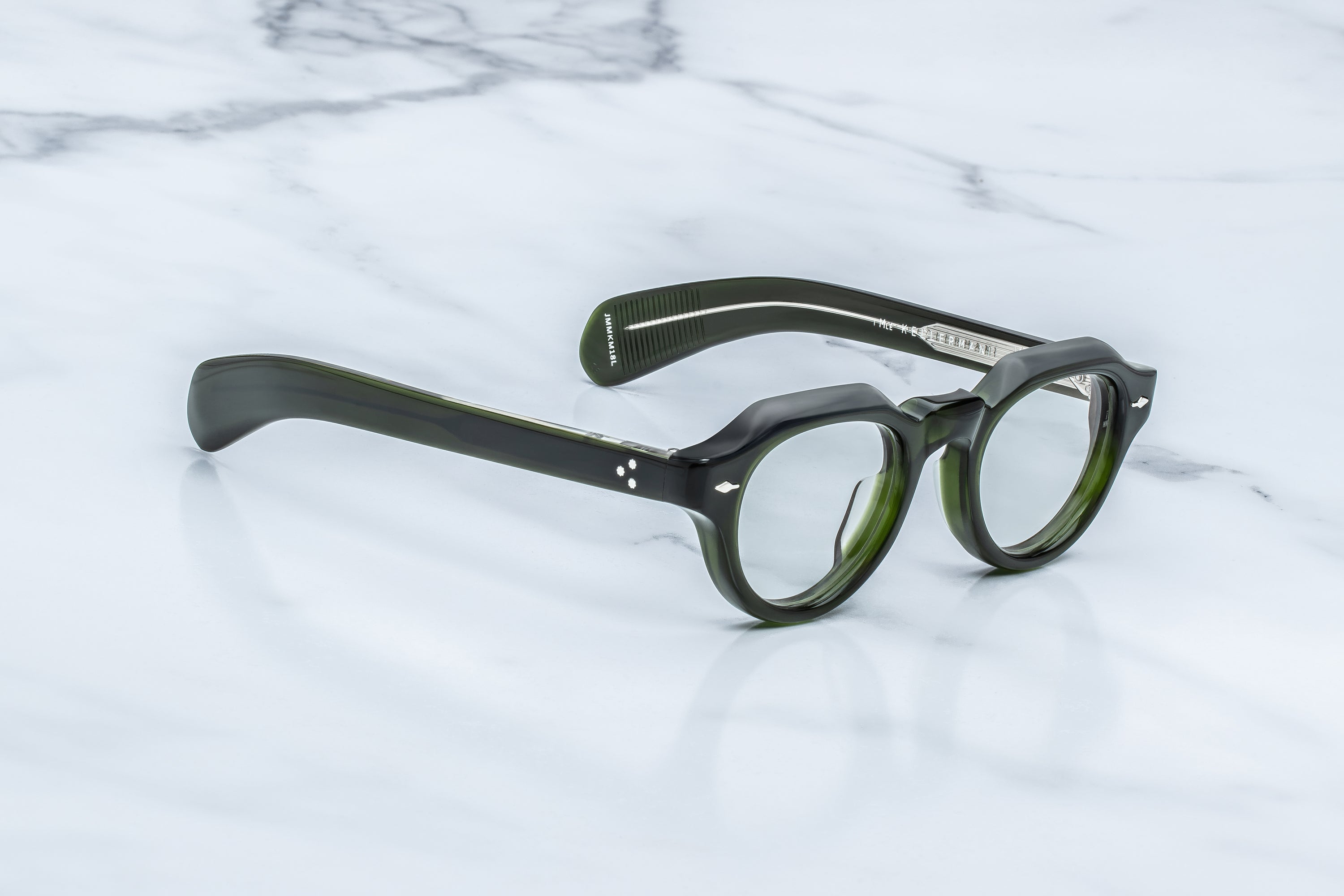 Round eyeglasses with thick dark green acetate frames and clear lenses, resting on a white marble surface.