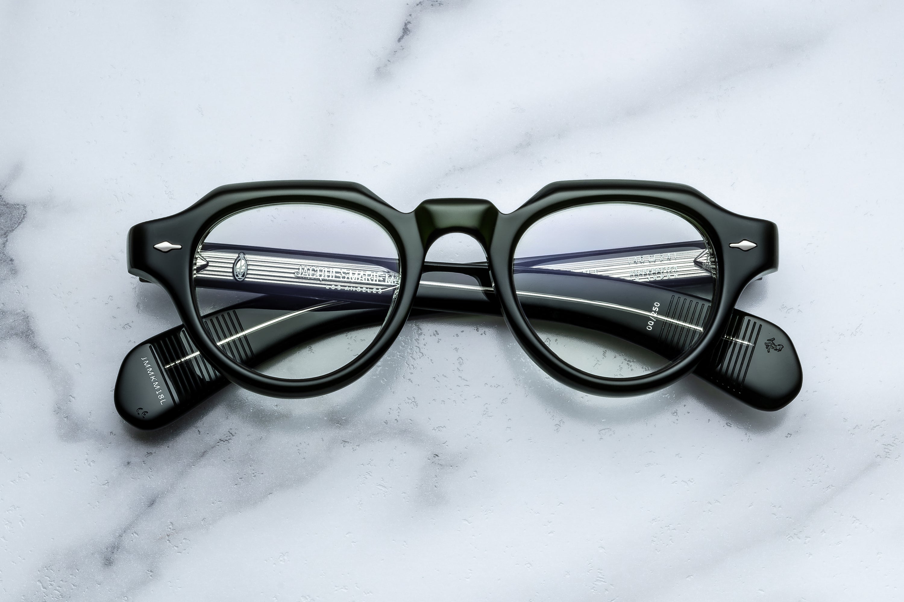 Green round-frame eyeglasses with clear lenses and striped temple arms, photographed from above on a white marble surface.