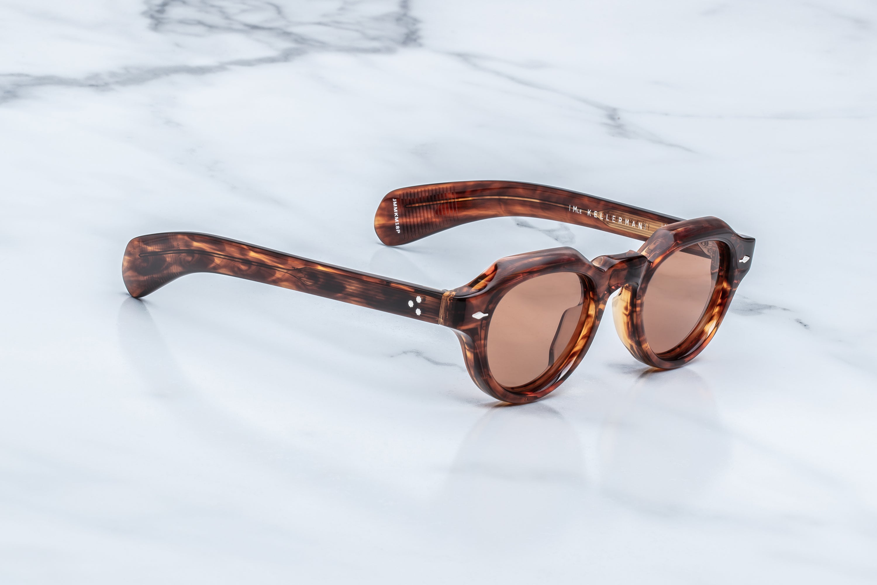 Retro-style sunglasses with a tortoiseshell acetate frame and brown tinted lenses, resting on a white marble surface.