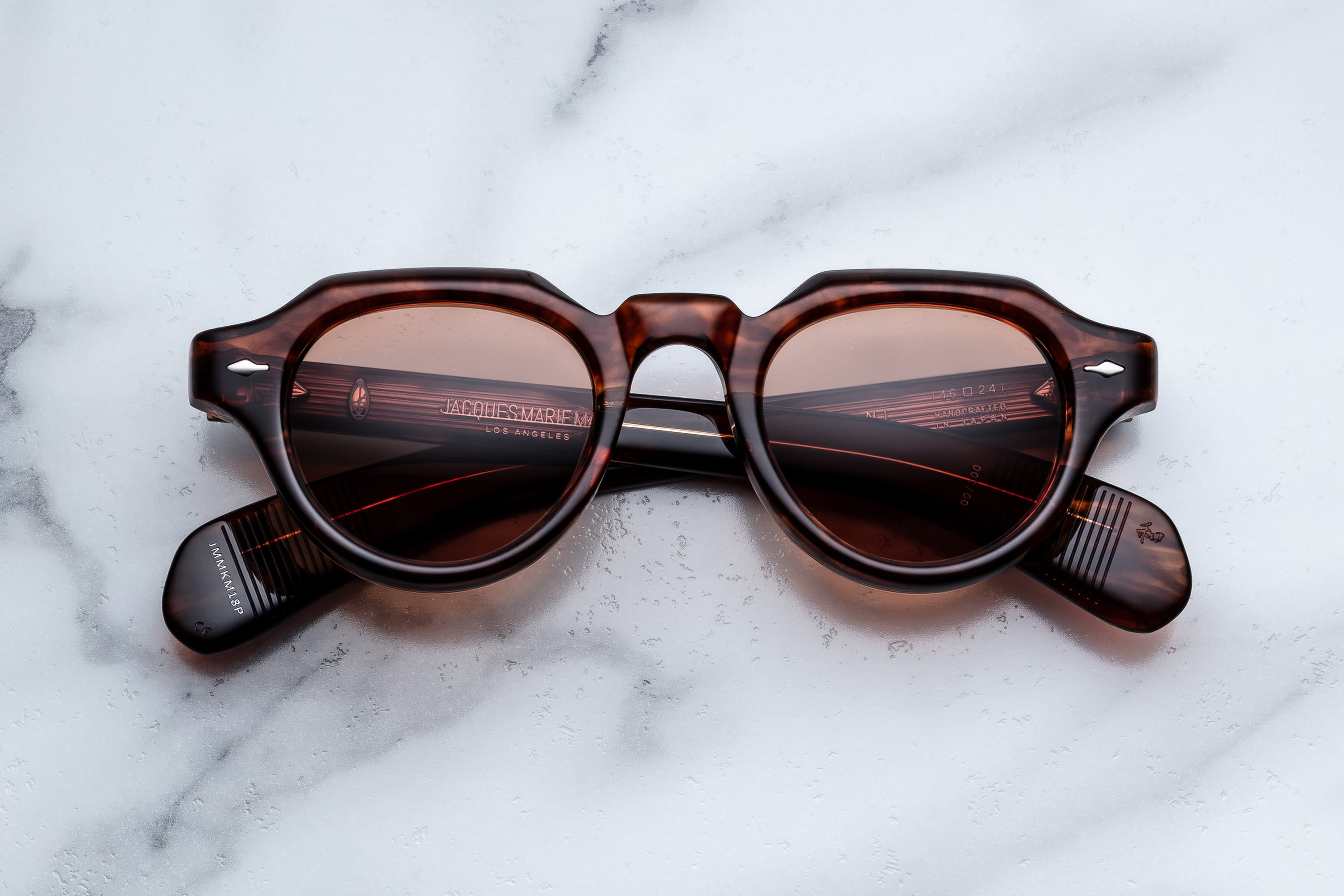 Round sunglasses with dark brown tortoiseshell frames and tinted lenses, resting on a white marble surface. 