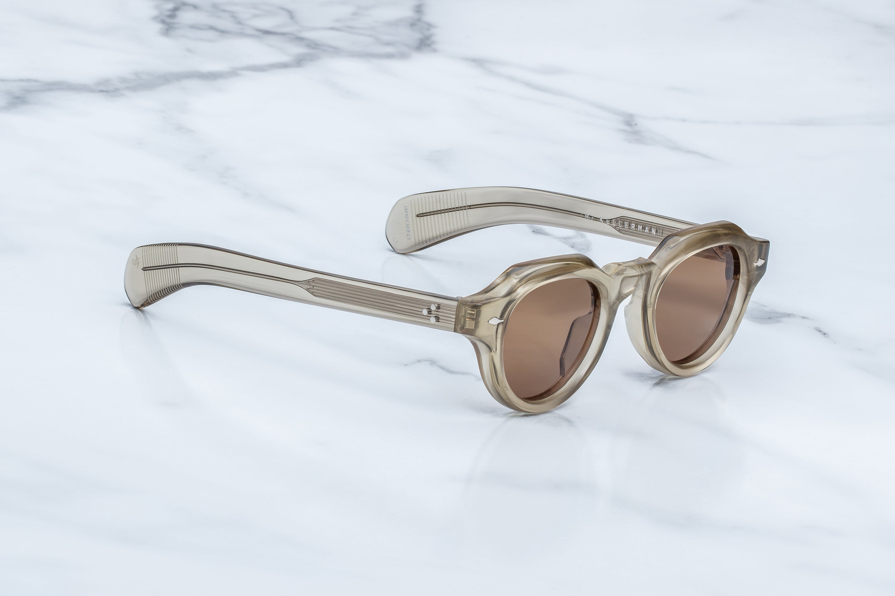 Round-frame sunglasses with translucent beige frames and brown lenses, resting on a white marble surface.
