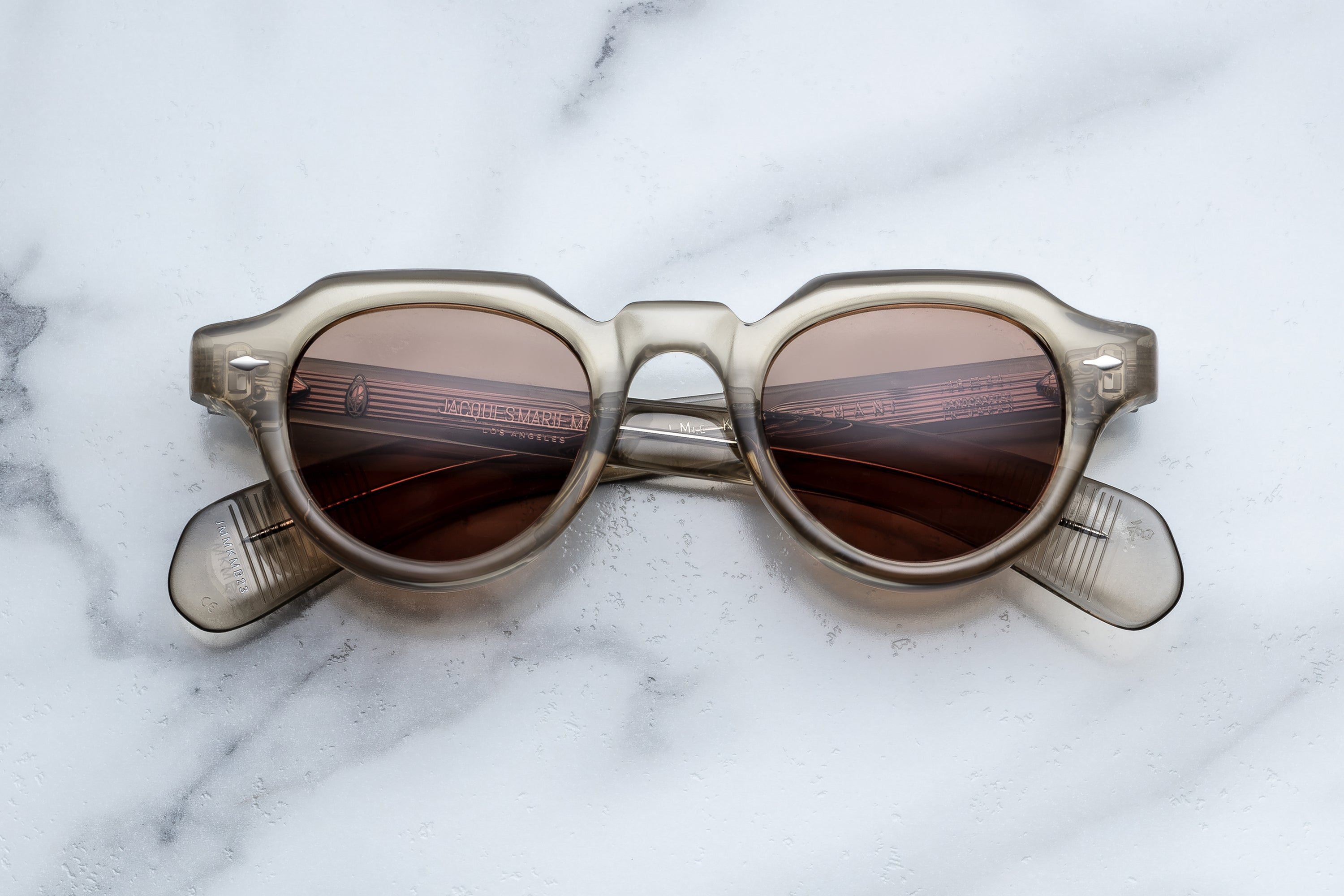 Oversized round sunglasses with a translucent smoky gray acetate frame and dark brown tinted lenses, resting on a white marble surface.
