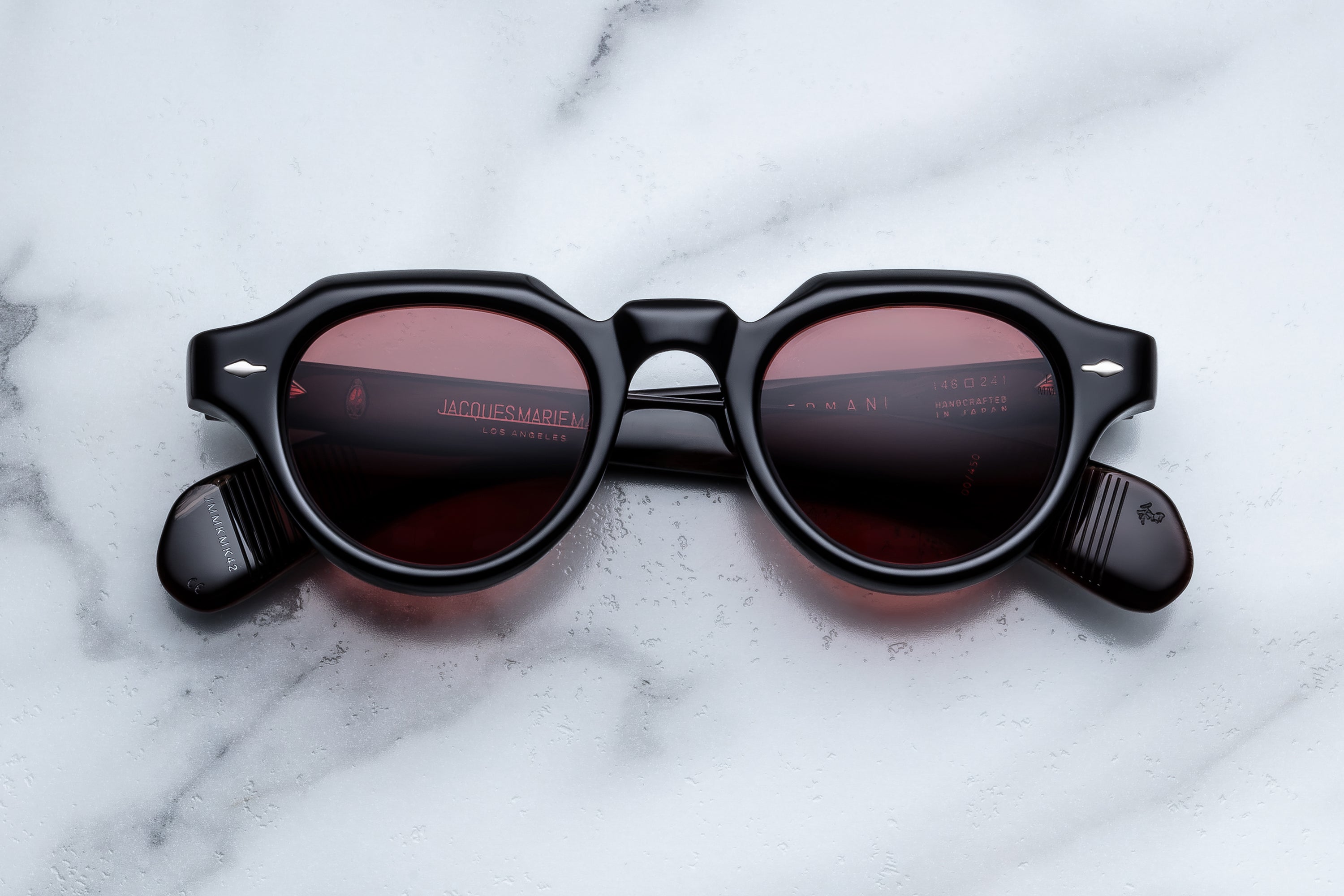 Round black sunglasses with dark tinted lenses, displayed on a white marble surface. 