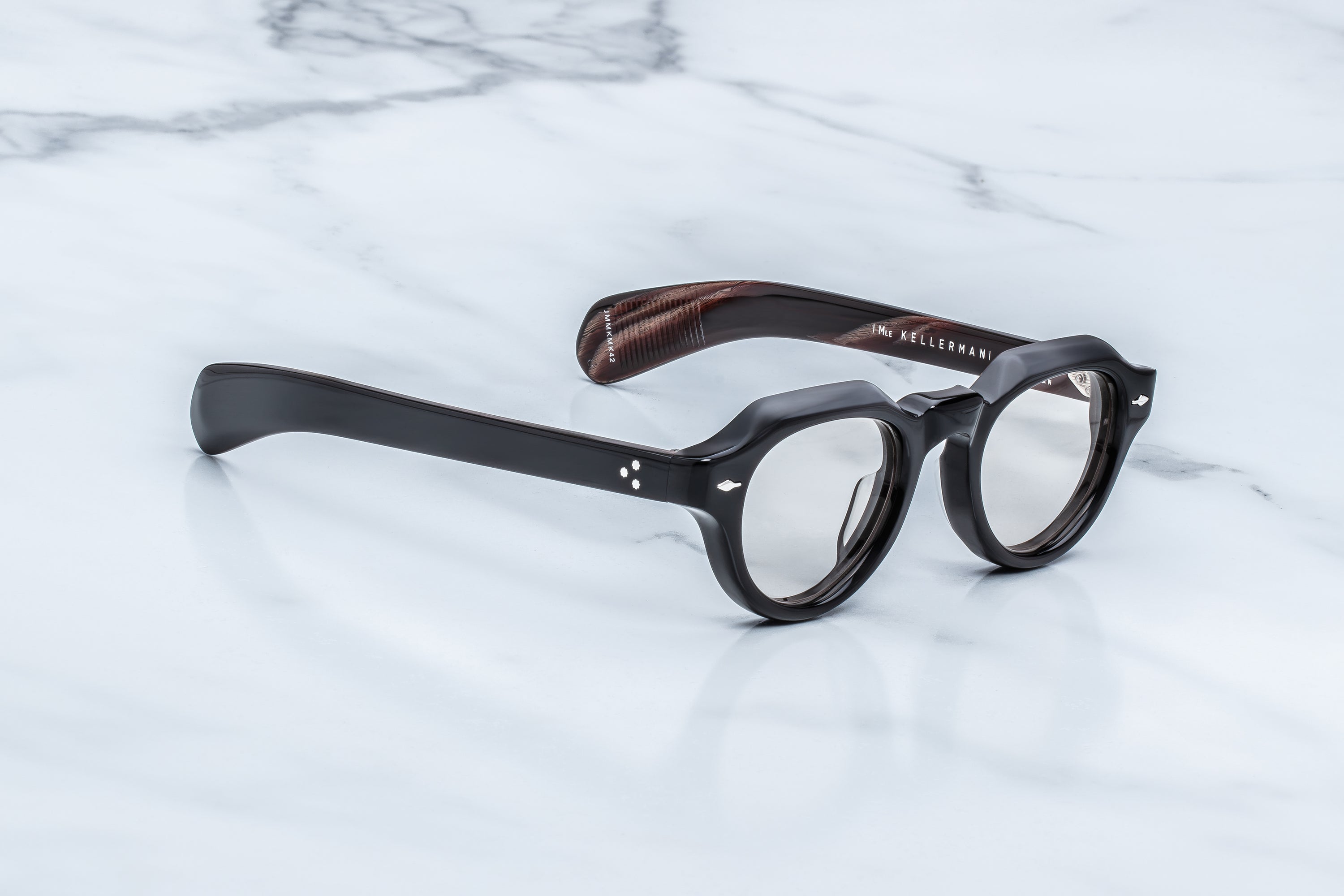Round black acetate eyeglasses with a brown wood-grain patterned inner temple, resting on a white marble surface.