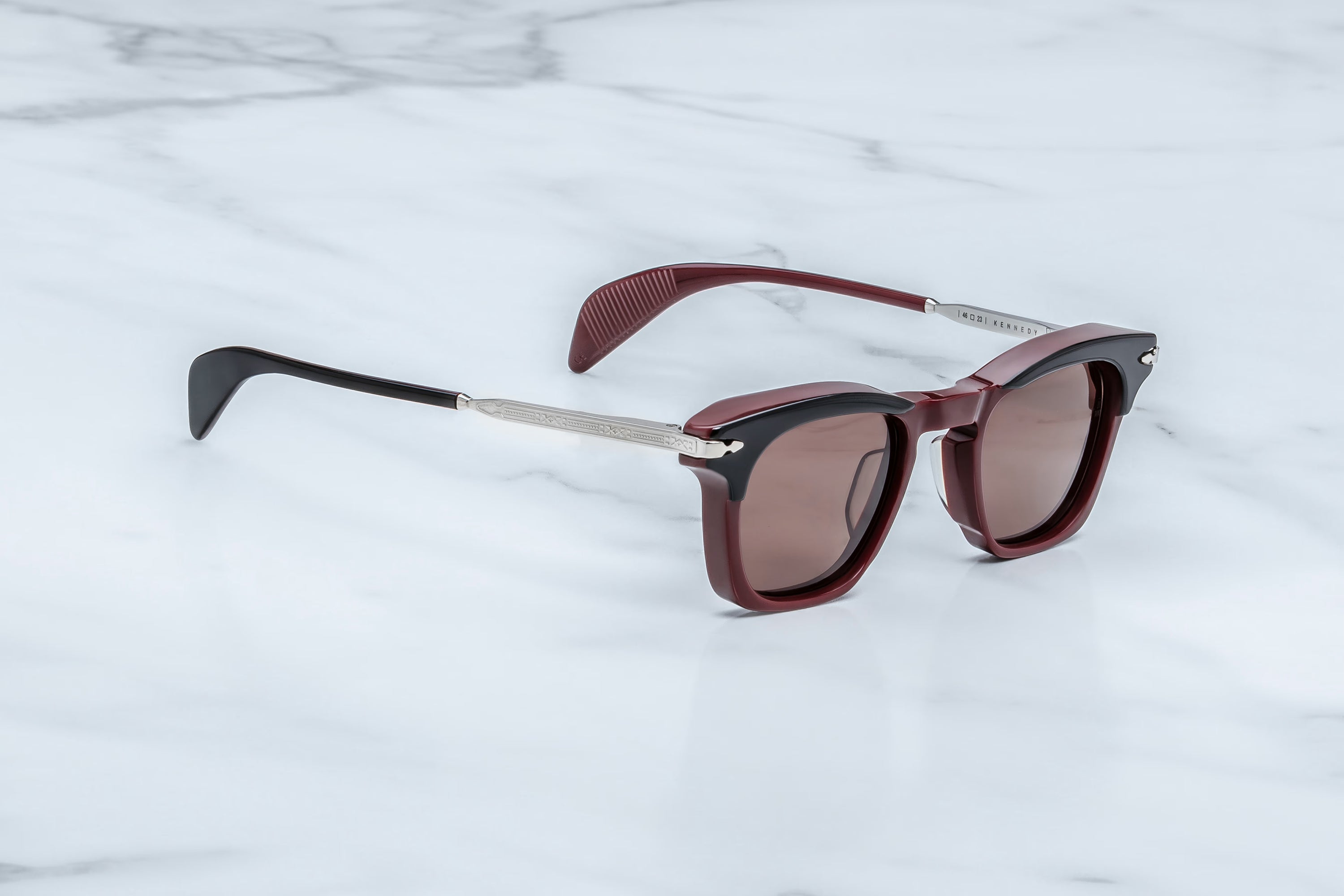 Sunglasses with maroon frame and dark lenses on a light gray background