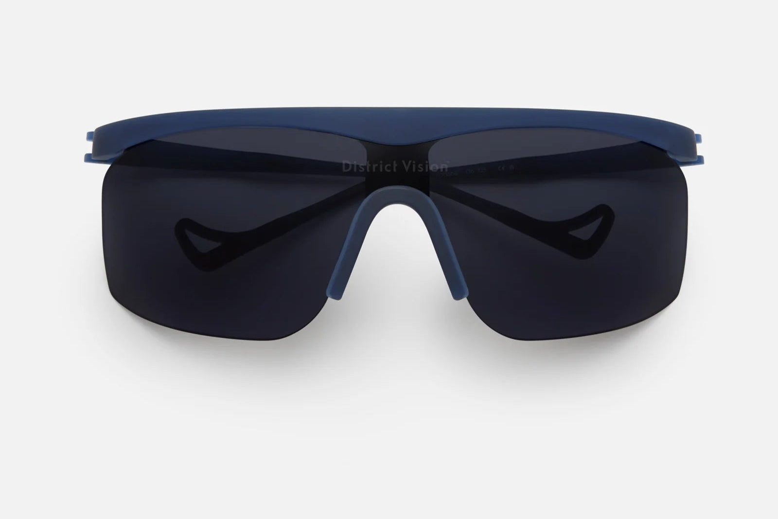 Featuring a sleek rectangular blade lens with advanced D+ lens technology, the District Vision Konoha Sun Sprinter from District Vision showcases dark wraparound sports sunglasses with a blue frame and nose pad, displayed against a plain white background. These shades combine cutting-edge performance with modern style.