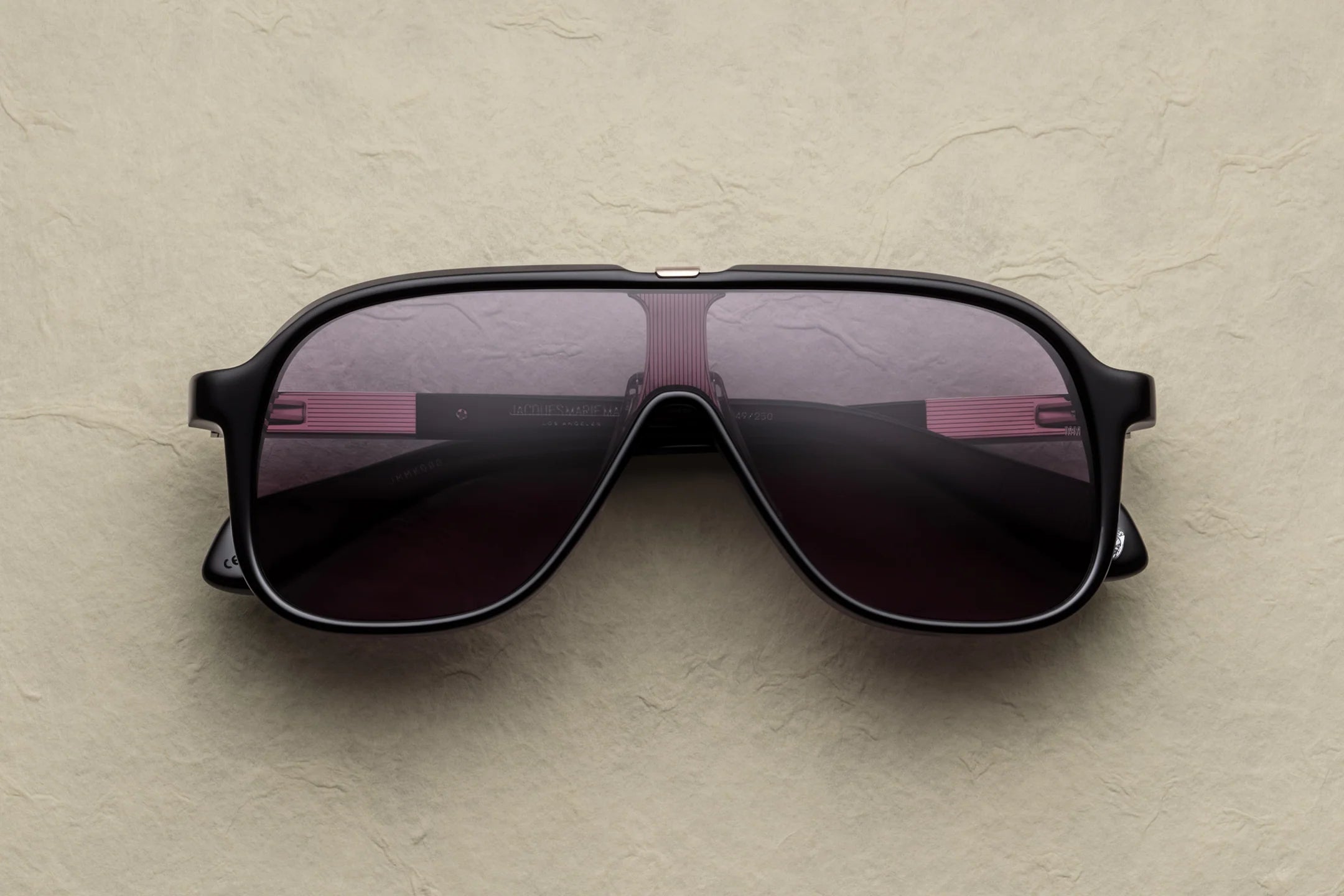 JMM Sunglasses with dark lenses on a beige surface