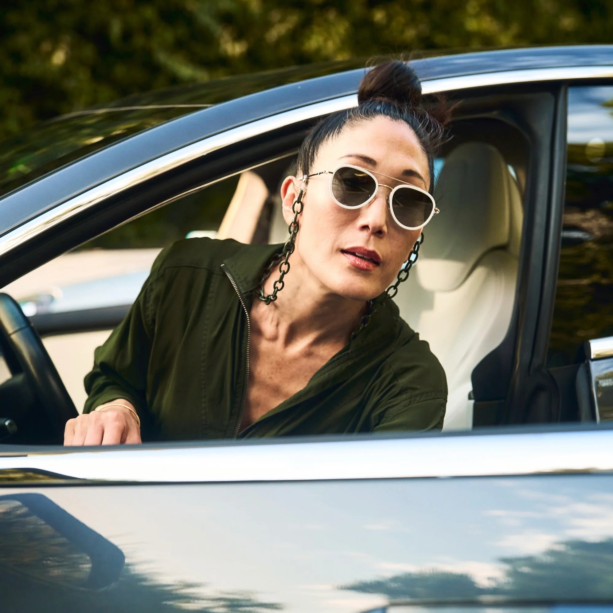 Woman wearing sunglasses and a green shirt sitting in a car.