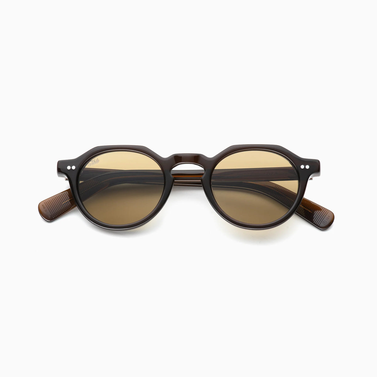 Akila Lola sunglasses by Akila, featuring round brown frames and dark tinted lenses, are shown from the front against a plain white background. The paddle-shaped temples are partially visible and folded outward, adding a subtle contemporary touch to the eyeglass frame design.