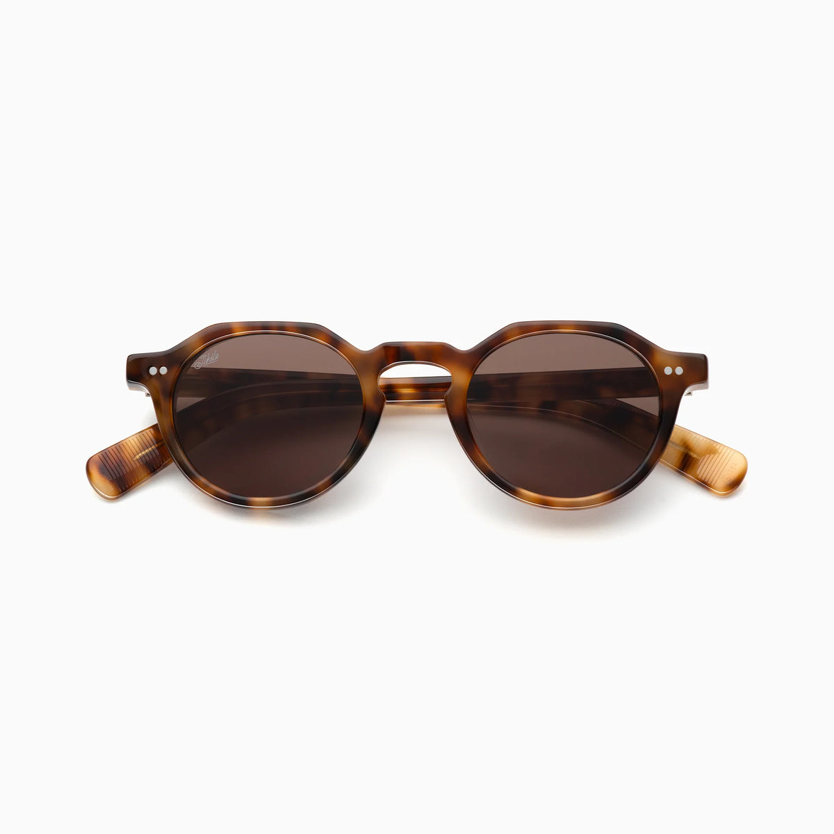 Akila Lola sunglasses by Akila, featuring a round tortoiseshell frame with dark brown lenses, are displayed on a white background. This contemporary model showcases a keyhole bridge, narrow fit glasses design, paddle-shaped temples, and two small dots accenting each upper corner.