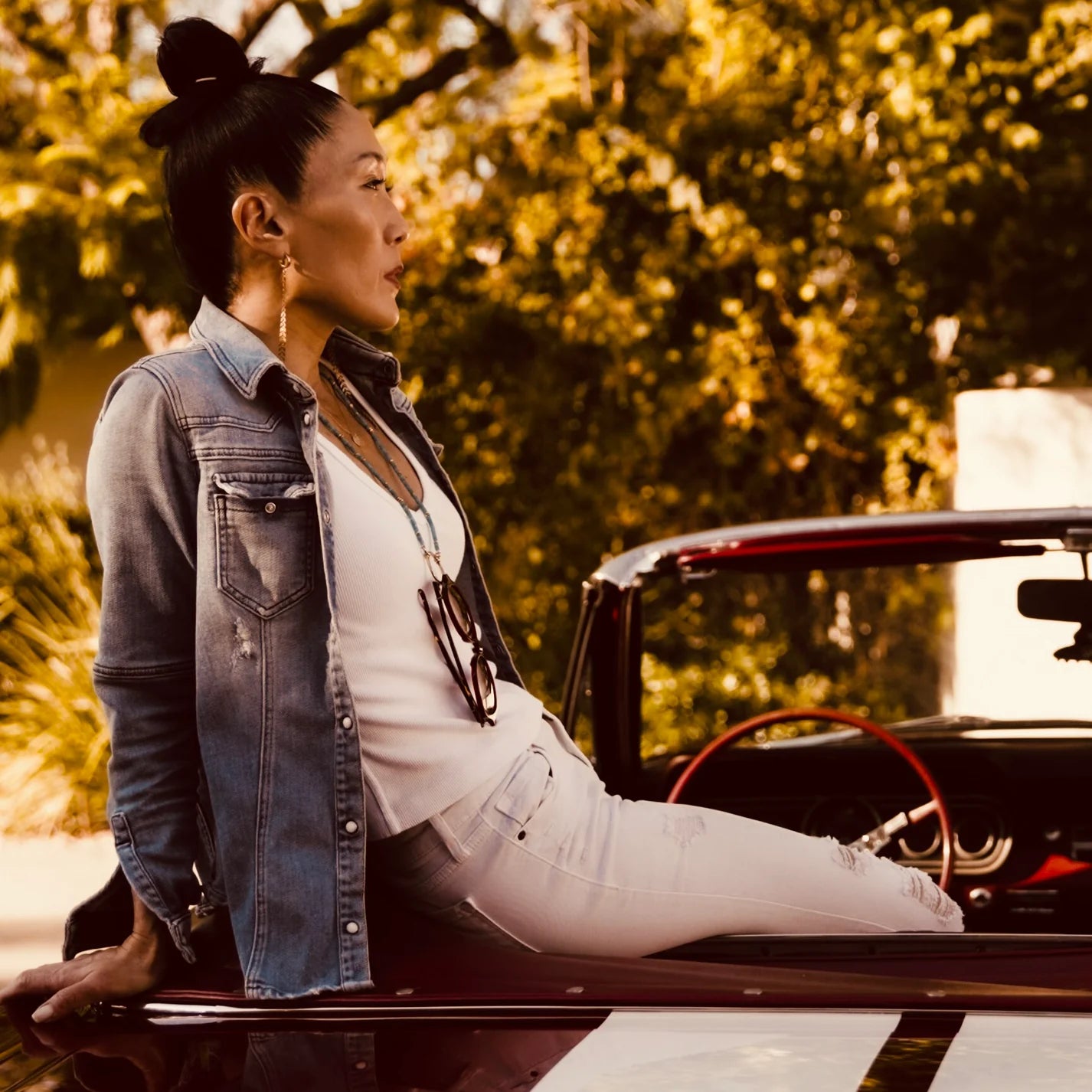 Woman sitting on a classic car with trees in the background