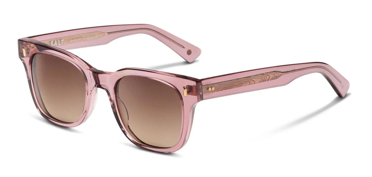 Translucent pink acetate sunglasses with brown gradient lenses, gold hinge accents, and patterned temple cores shown at an angled side view on a white background.