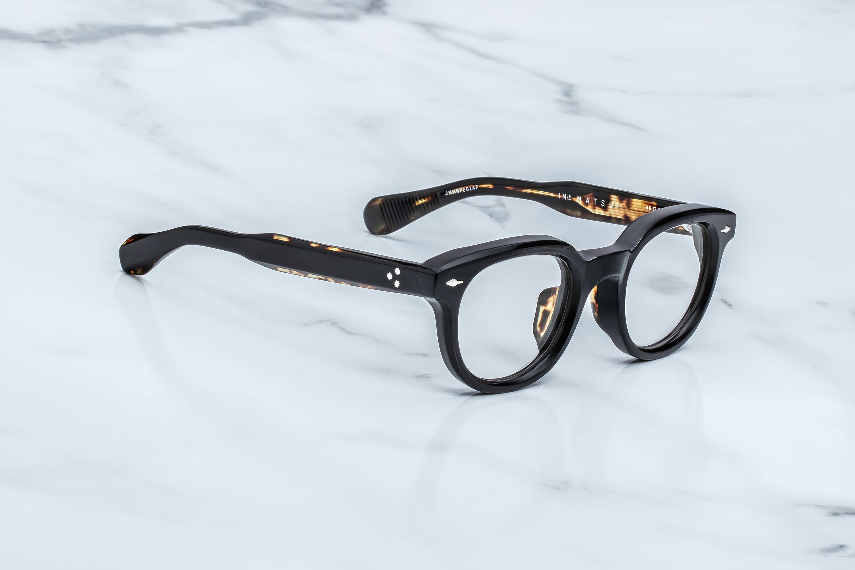 Round eyeglasses with black frame and tortoiseshell accents on a light gray background