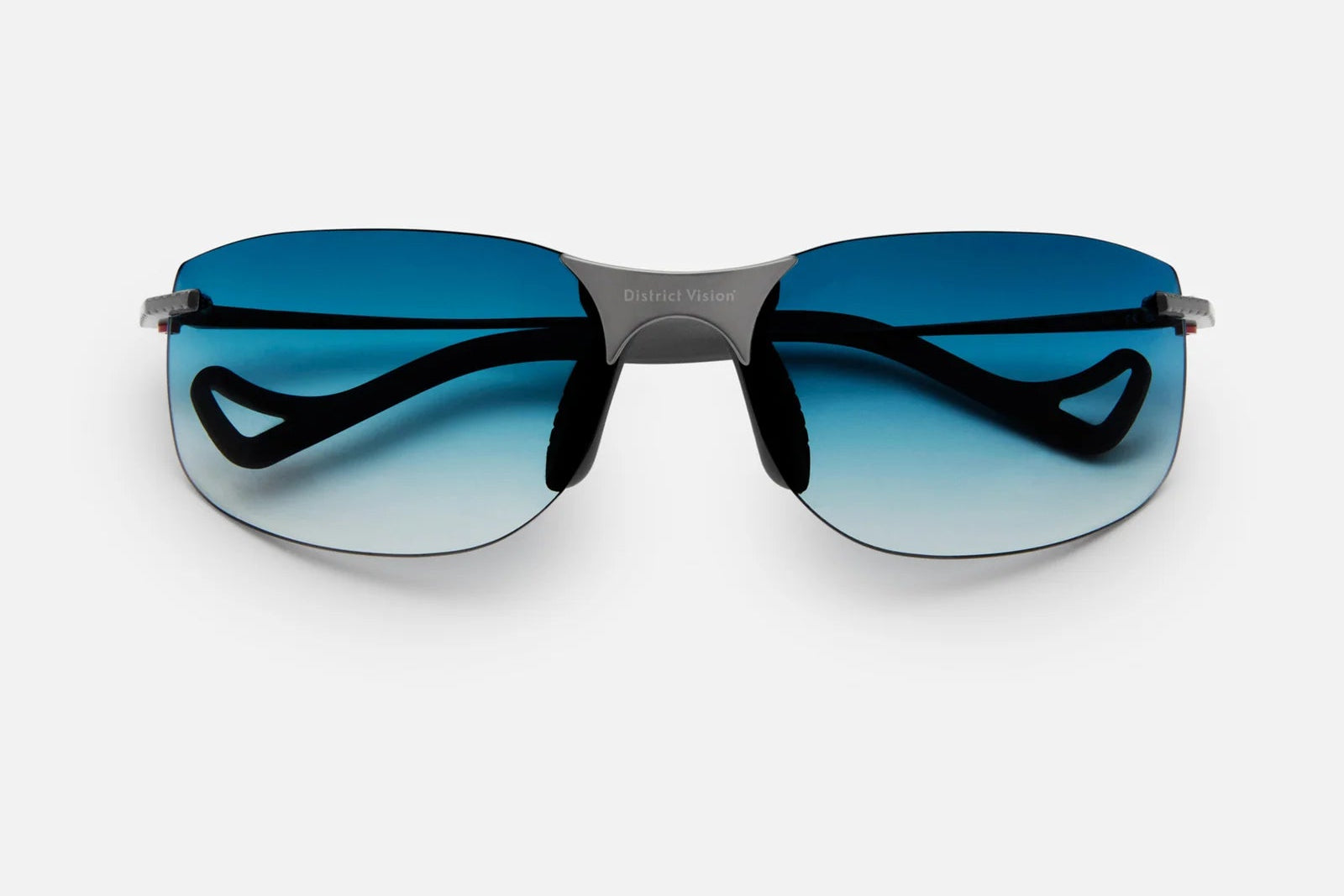 The District Vision Miho Windstream Ti by District Vision are rimless sunglasses with blue gradient lenses and black arms, offering a customizable fit and lightweight titanium construction, shown against a plain white background.