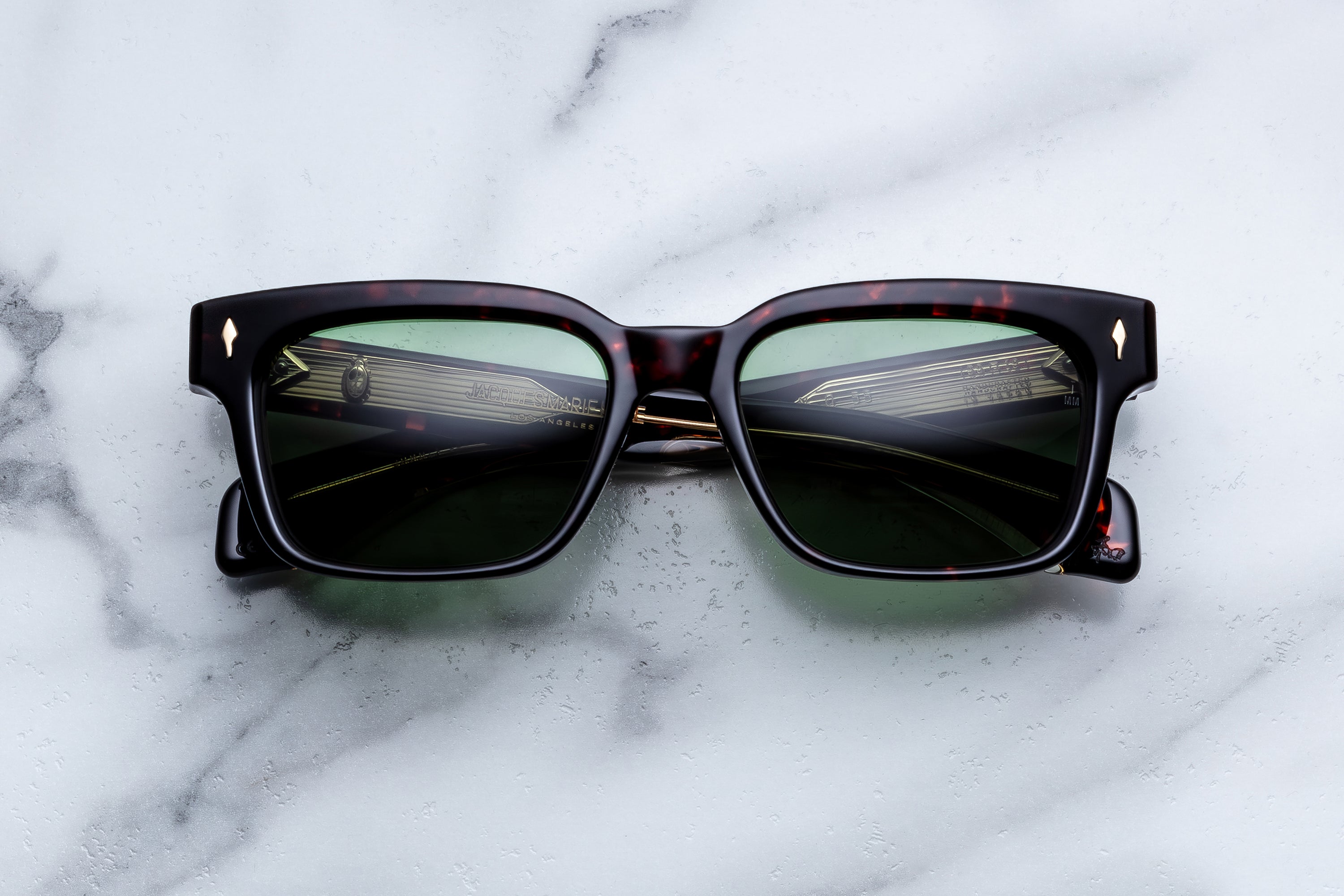 A pair of square-frame sunglasses with dark tortoiseshell acetate frames and dark green lenses, resting on a white marble surface.