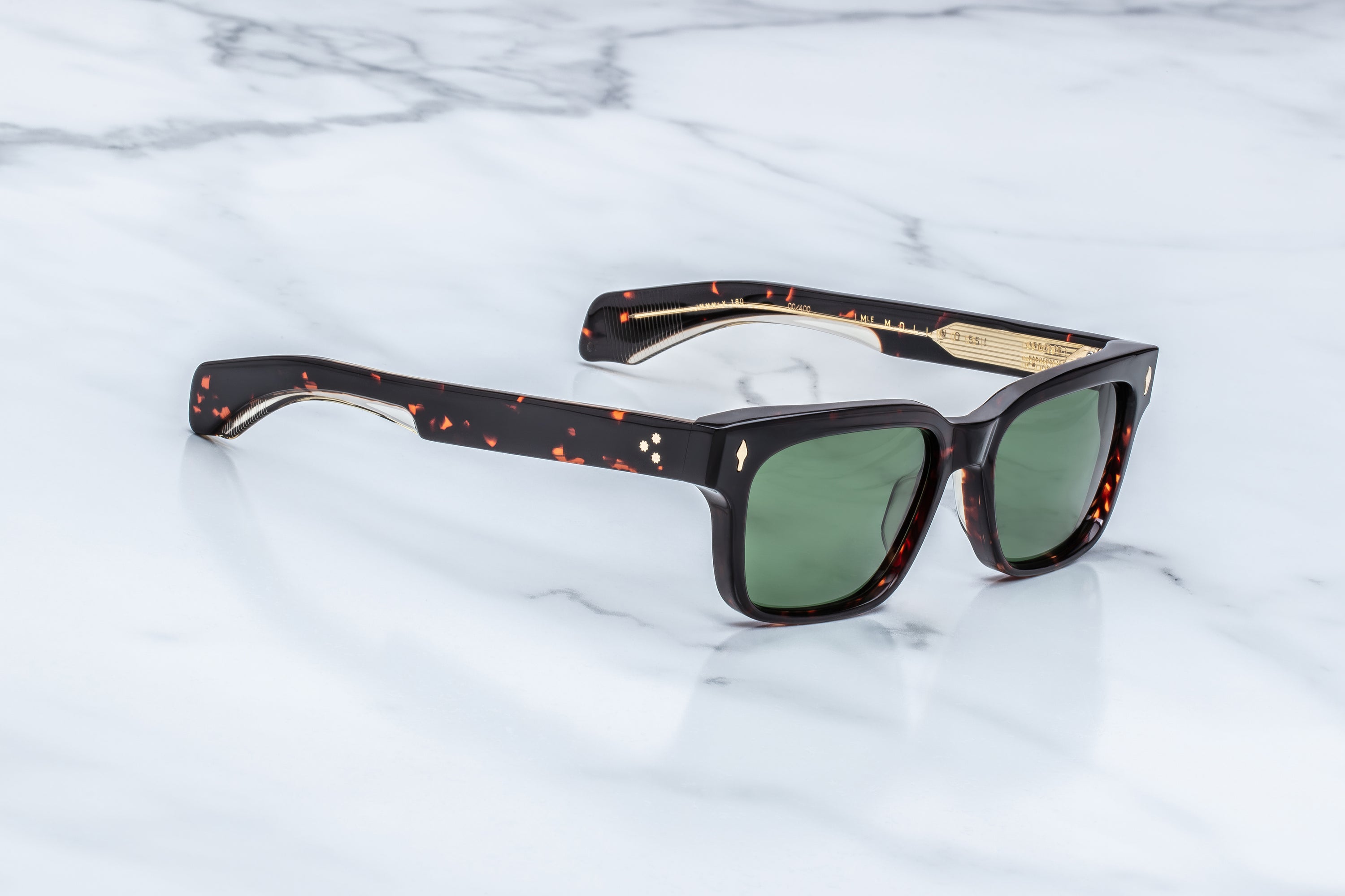 A pair of sunglasses with dark tortoiseshell frames and green lenses, resting on a white marble surface.