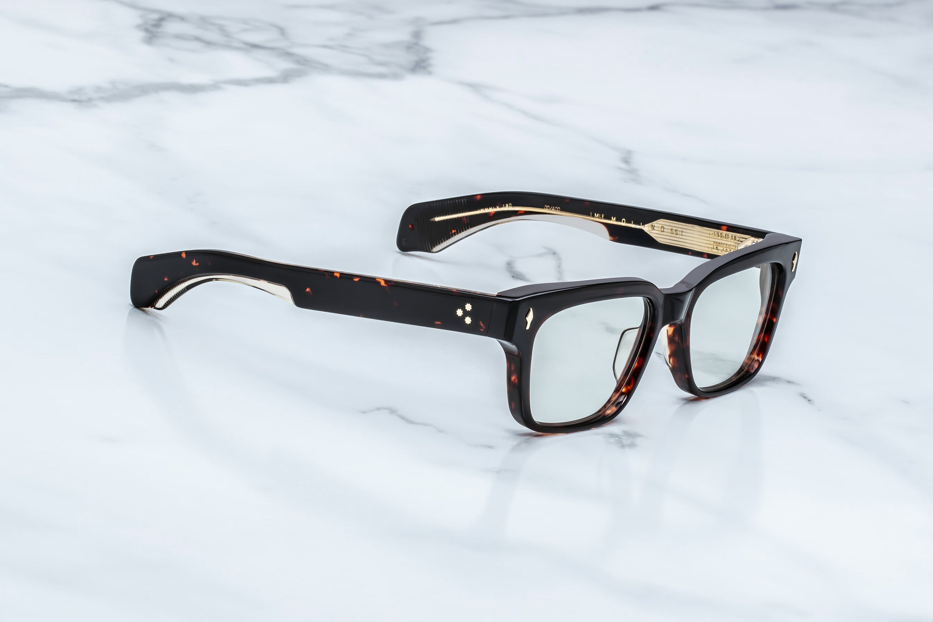 A pair of square-frame eyeglasses with dark tortoiseshell acetate arms and temples, resting on a white marble surface.