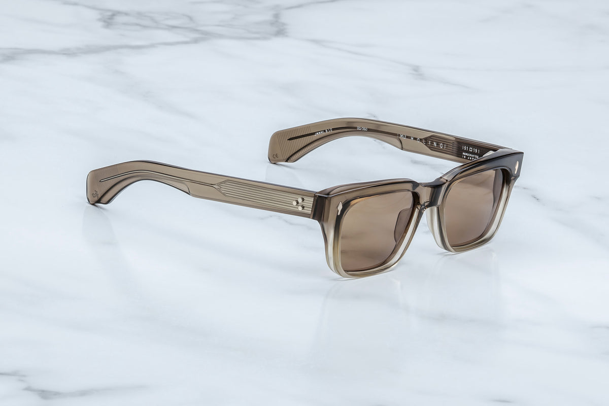 Jacques Marie Mage Molino rectangular sunglasses with thick transparent frames and tinted lenses rest on a white marble surface, their bold lines reflecting the signature style of Italian designer Carlo Mollino.