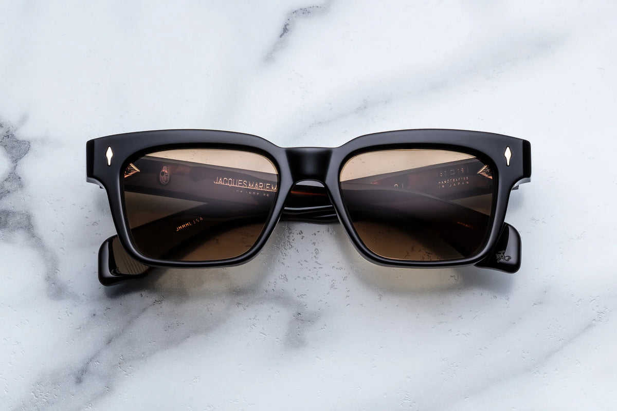Jacques Marie Mage Molino black rectangular sunglasses with light brown tinted lenses and gold-tone arrow-shaped rivets, inspired by the Carlo Mollino design aesthetic.