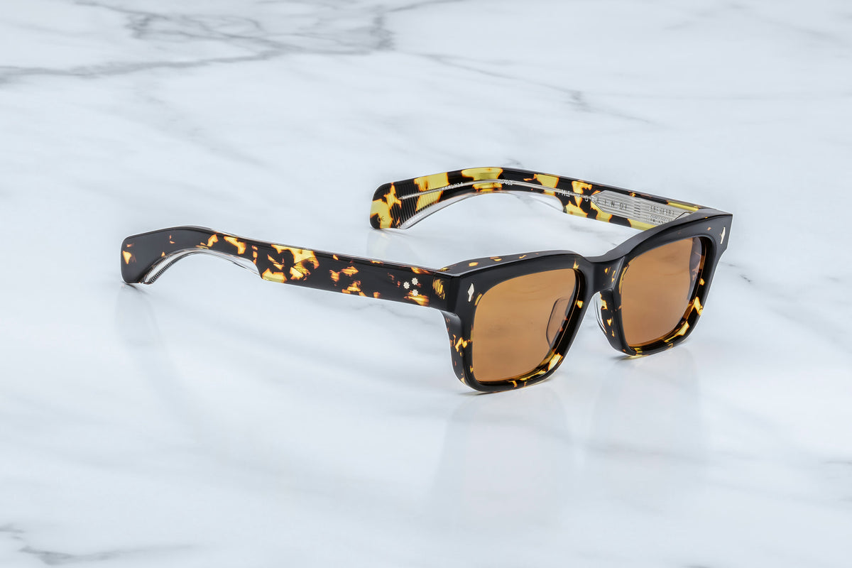 Jacques Marie Mage Molino sunglasses, featuring a tortoiseshell pattern, a distinctive rectangular shape, and brown lenses, are displayed on a white marble surface, reflecting the sophisticated style of Italian designer Carlo Mollino.