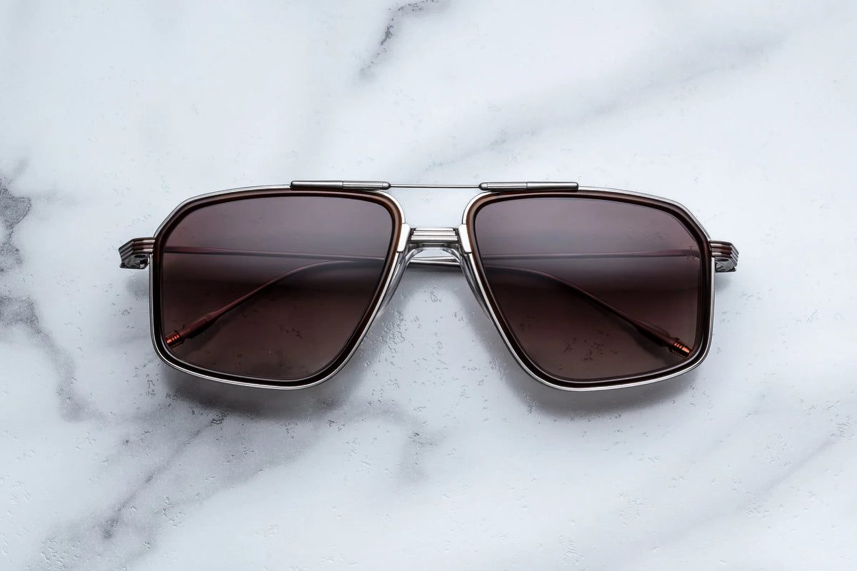 Jacques Marie Mage Yellowstone VII: Moran In Mammoth navigator sunglasses with silver frames and brown lenses resting on a white marble surface.