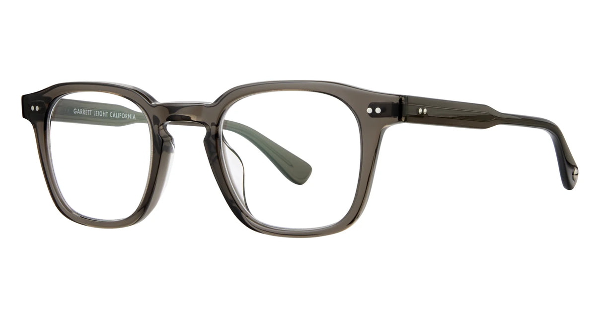The Garrett Leight Verdugo eyeglasses by Garrett Leight feature a translucent gray rectangular frame with gently rounded edges, distinctive metal rivets on the front corners and temples, and green-tinted temple tips. Inspired by the signature GLCO sunglasses style, these glasses are designed to provide UV protection for your eyes.