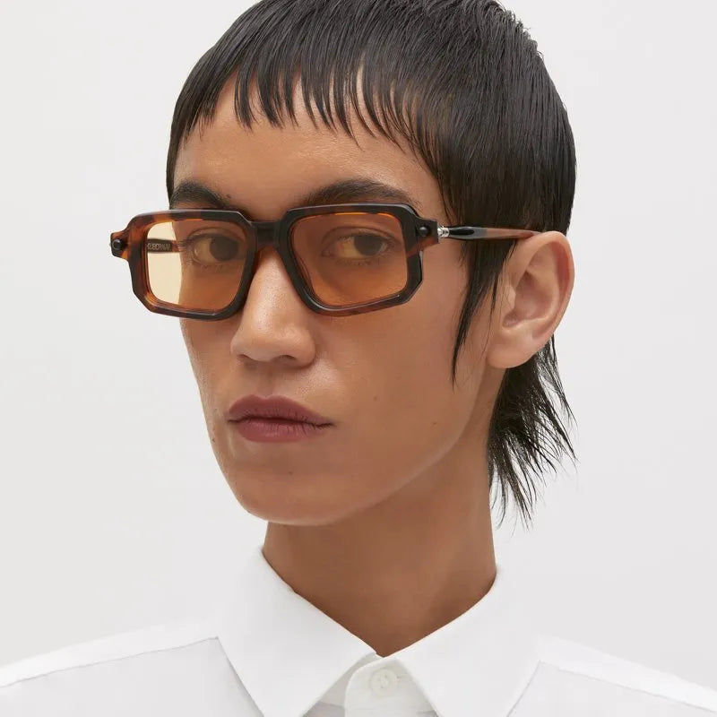 Person wearing brown glasses and a white shirt on a light gray background