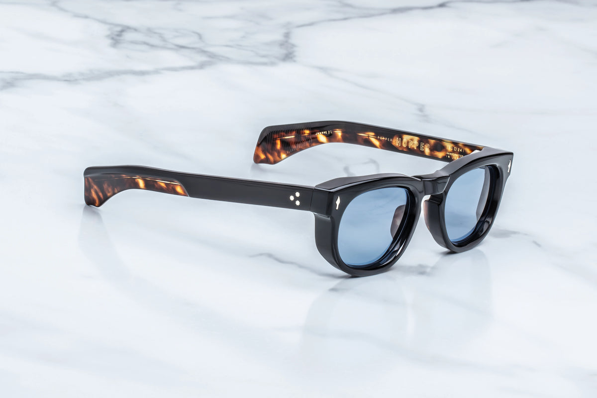 Jacques Marie Mage A Decade of Hopper: Pepper sunglasses featuring a black rectangular frame, light blue lenses, and tortoiseshell temple tips.