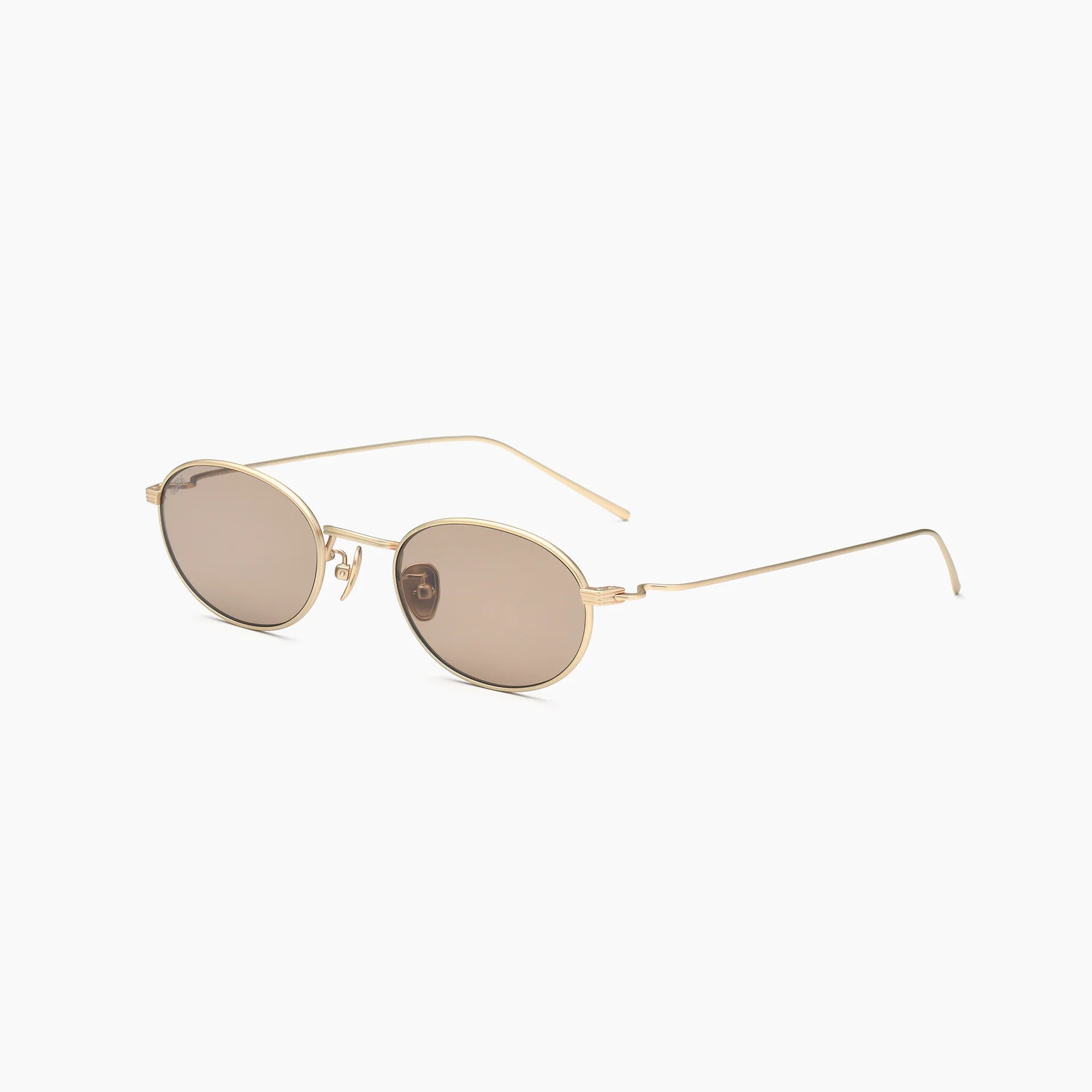 Oval gold metal-frame sunglasses with brown-tinted lenses, adjustable nose pads, and slim wire temples, shown at an angled side view on a white background.