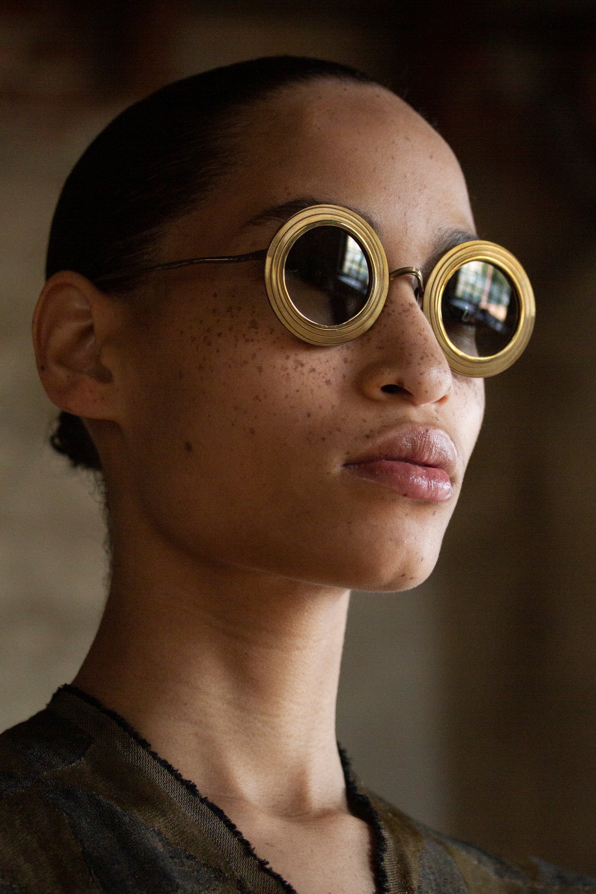 Model wearing oversized round RIGARDS sunglasses with textured gold-tone rims and dark lenses, photographed from a three-quarter angle.