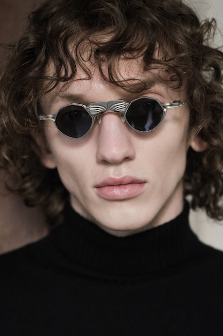 Model wearing silver RIGARDS round sunglasses with dark lenses and an ornate sculptural bridge, photographed in a close-up portrait.