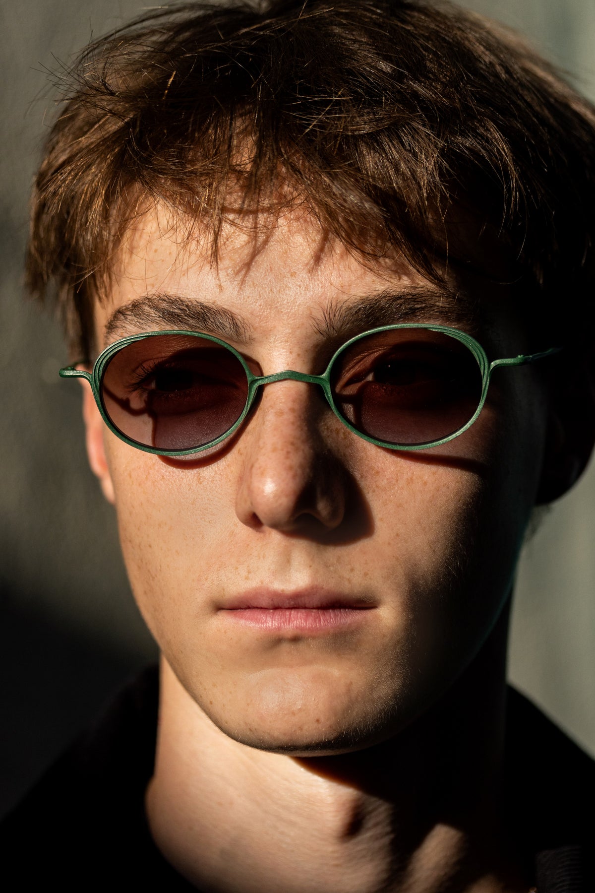 Model wearing green RIGARDS oval sunglasses with brown gradient lenses, photographed in dramatic sunlight.