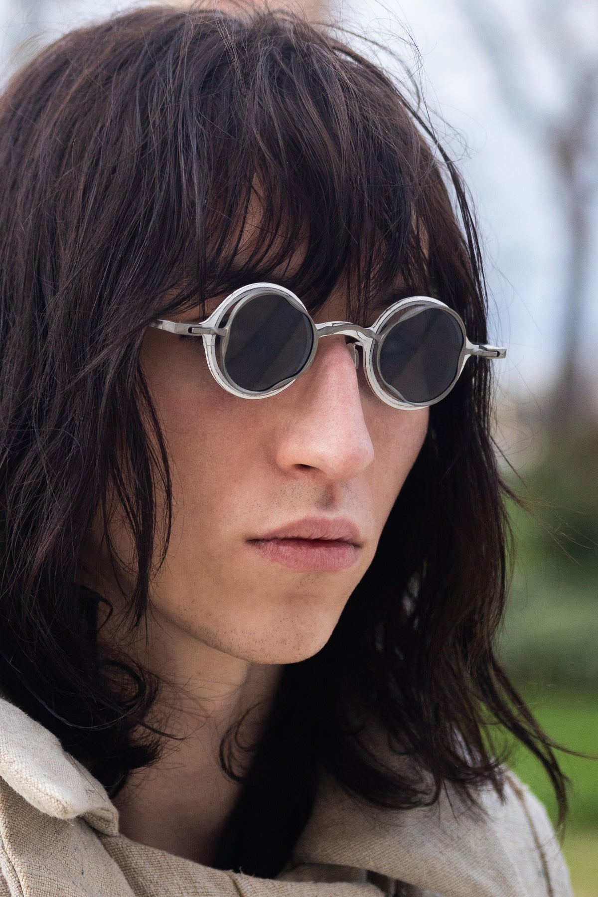 Model wearing silver RIGARDS round sunglasses with dark lenses and sculptural layered rims, photographed outdoors from a three-quarter angle.