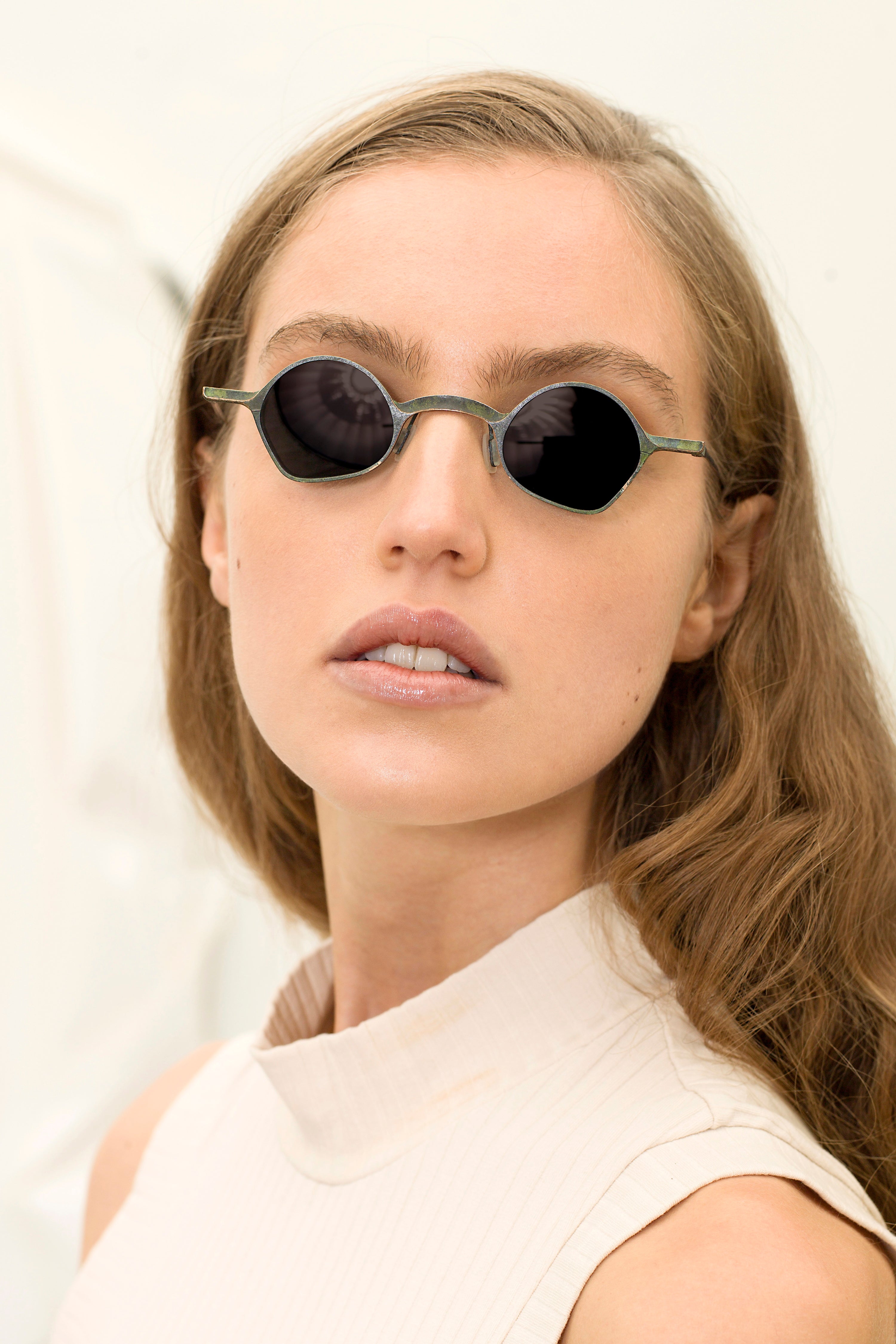 Model wearing RIGARDS geometric sunglasses with textured green metal rims and dark lenses, photographed in a close-up portrait.