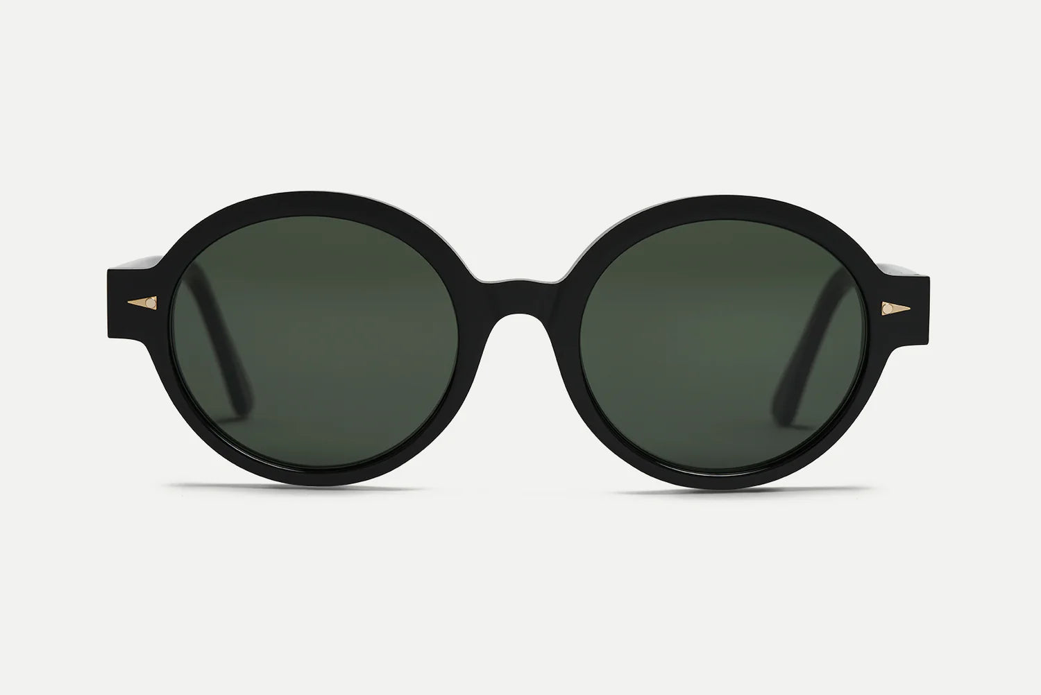 Oval sunglasses with a thick black frame and dark green lenses, featuring small gold geometric accents on the temples, shown against a light gray background.