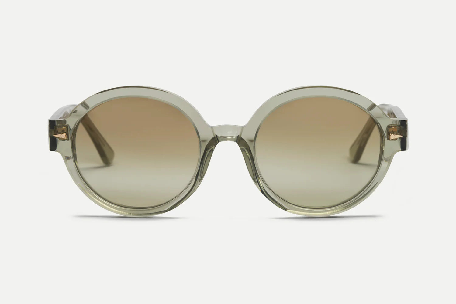 Oversized round sunglasses with a translucent smoky olive-green frame and gradient brown lenses, shown against a light gray background.