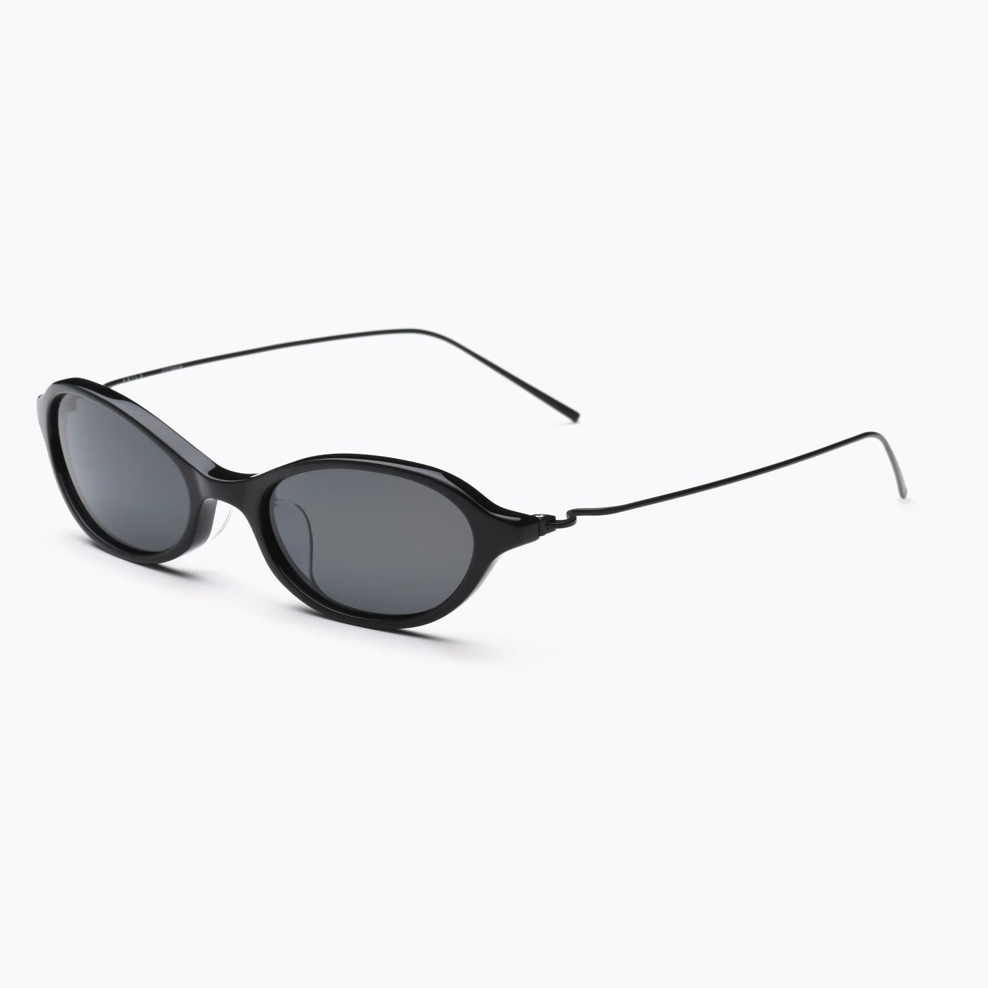 Black oval sunglasses with dark gray lenses and thin black metal temples, shown at an angled side view on a white background.