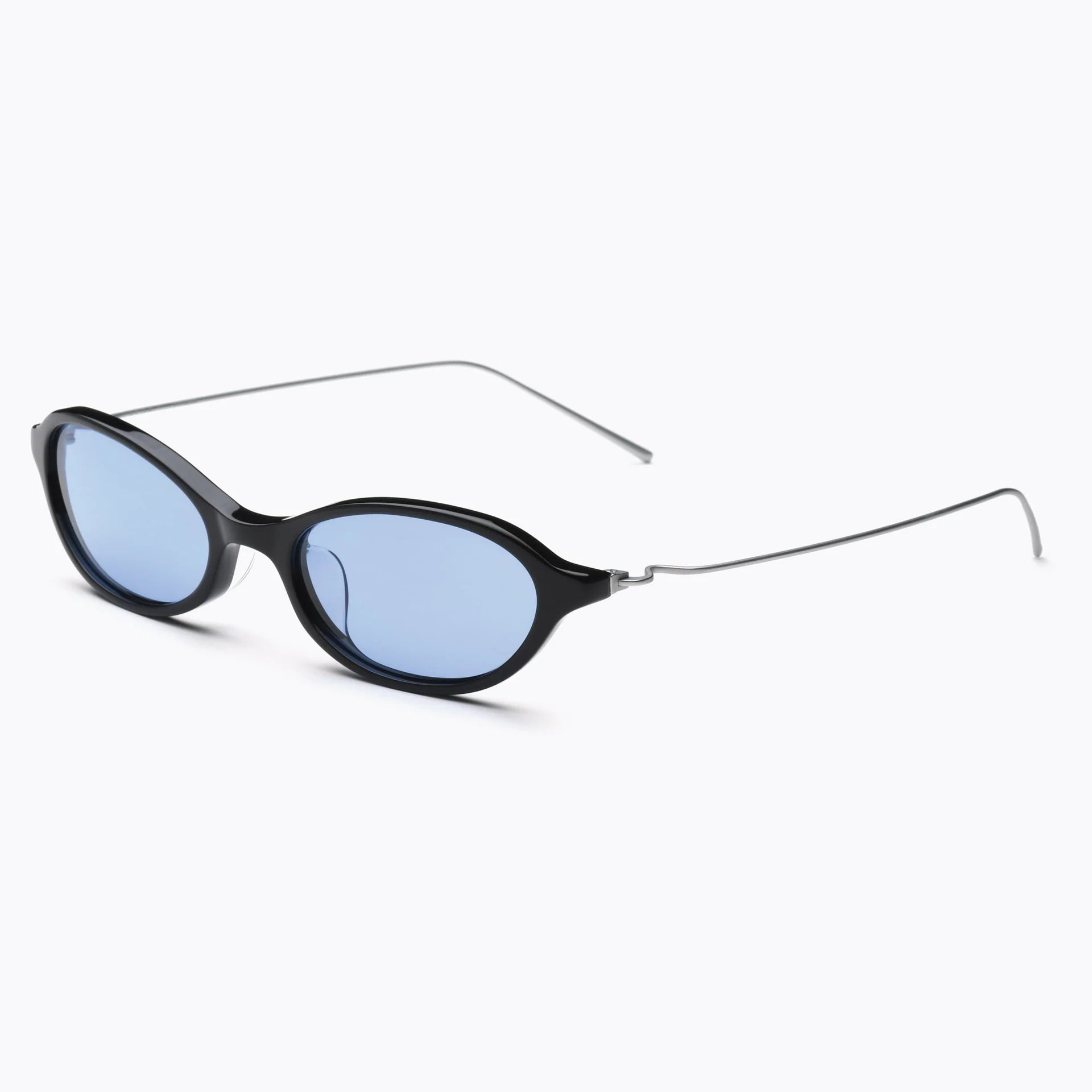 Black oval sunglasses with light blue-tinted lenses and thin silver metal temples, shown at an angled side view on a white background.