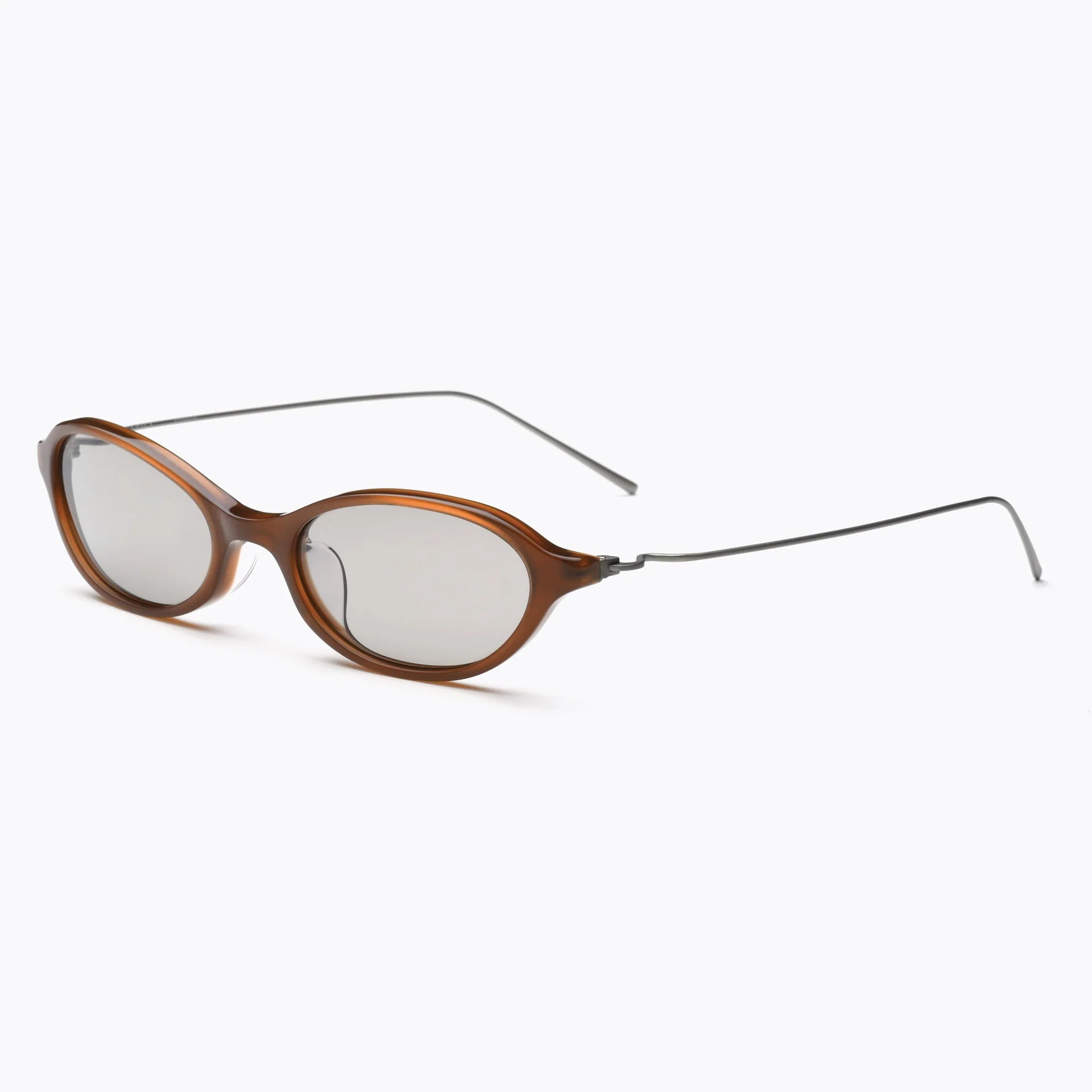 Brown oval sunglasses with light gray-tinted lenses and thin silver metal temples, shown at an angled side view on a white background.