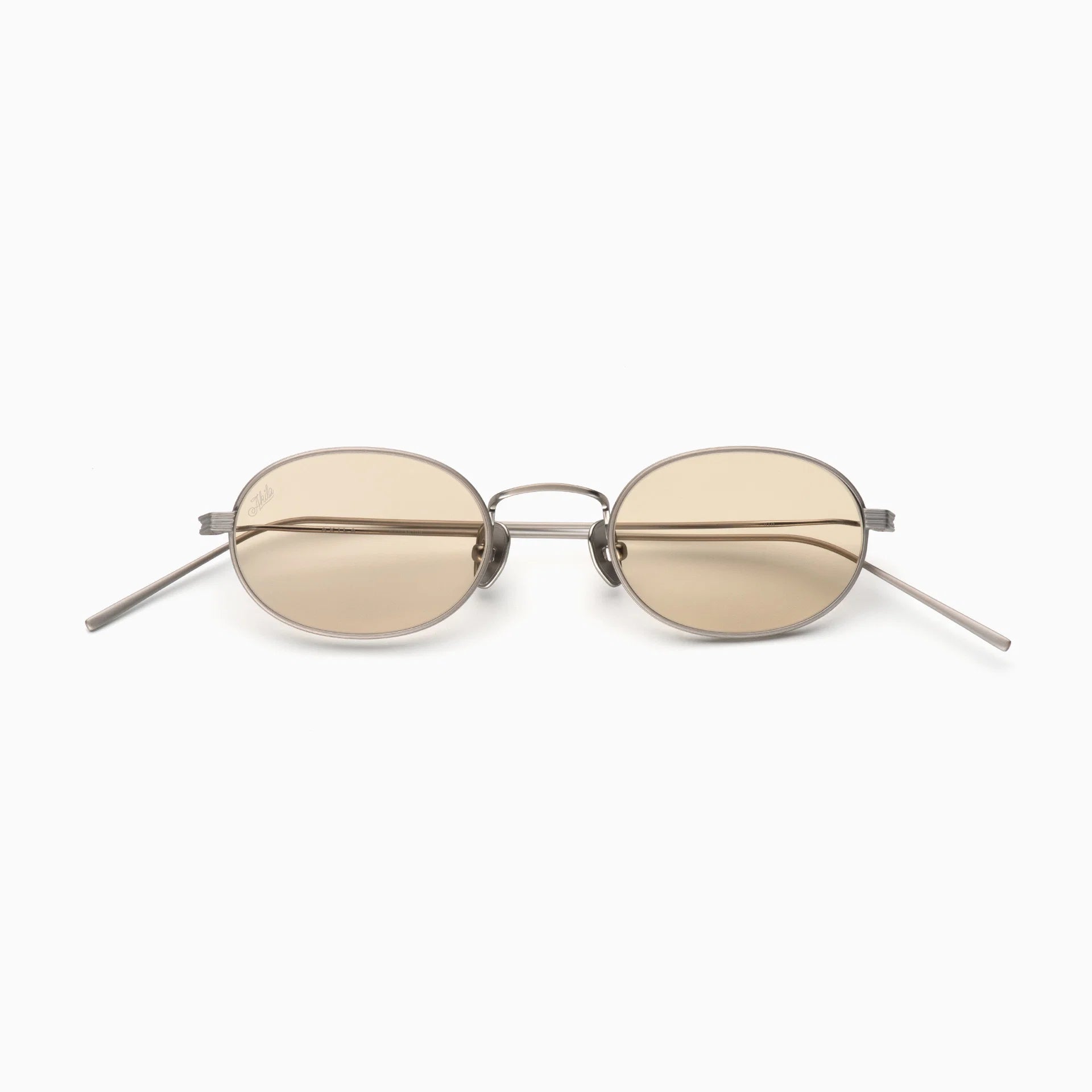 Akila Rio sunglasses by Akila feature an oval shape with thin metal titanium frames and light brown tinted lenses, shown on a white background. Inspired by Akila’s signature style, these glasses have straight temples that angle slightly outward for a contemporary look.
