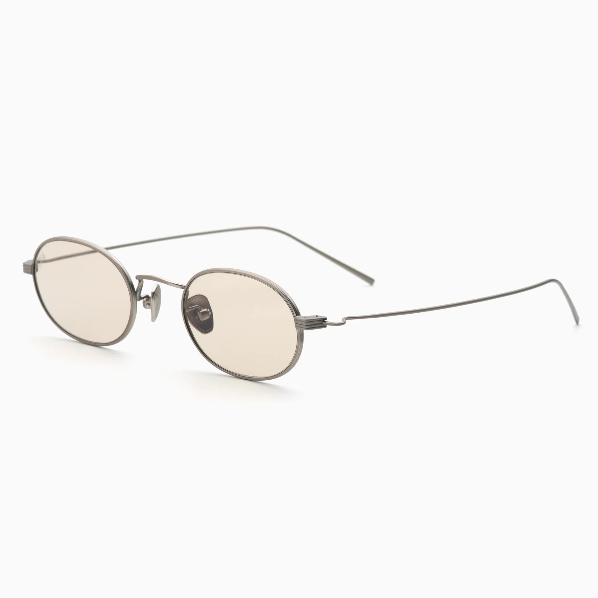 The Akila Rio by Akila are round, thin titanium glasses with an elegant oval frame, light beige lenses, and minimalist wire arms, displayed on a white background.