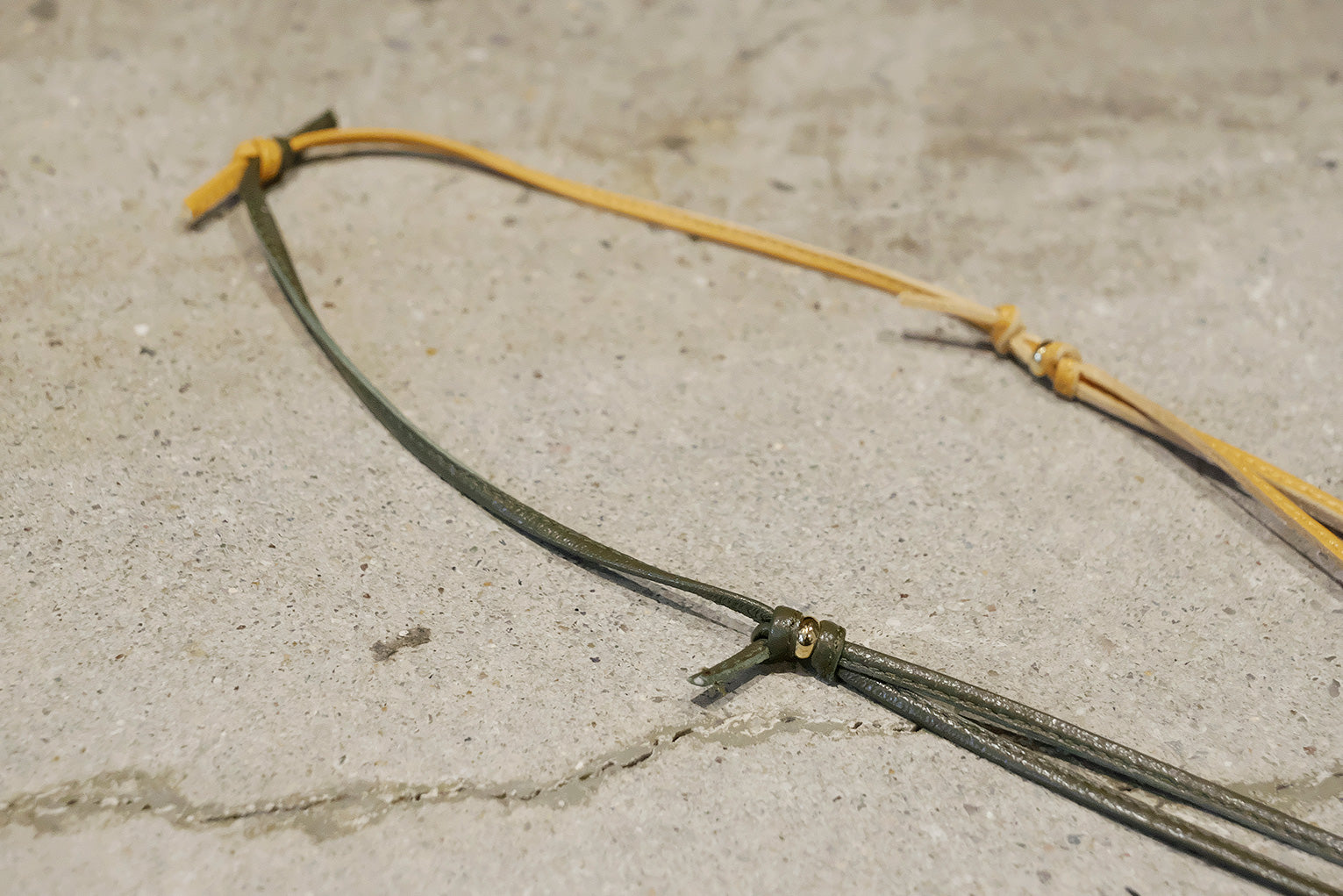 Close-up of a leather cord with yellow and green ends on a concrete surface
